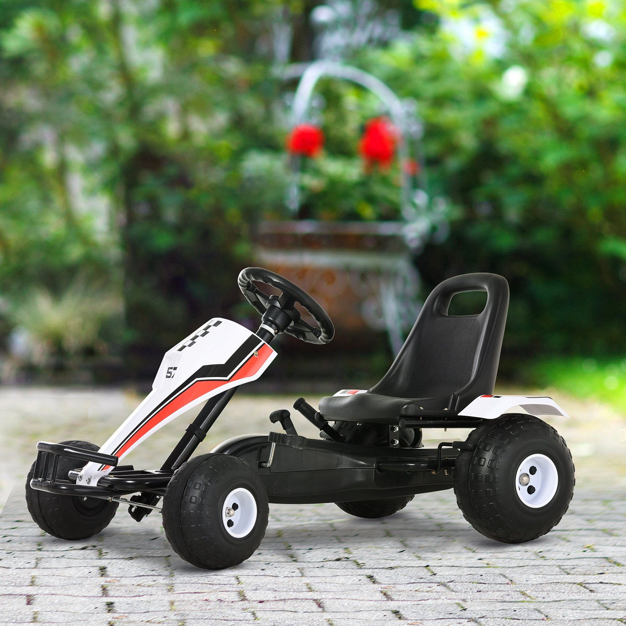 Un go-kart bianco e nero con dettagli rossi si trova su un sentiero lastricato con sfondo verde da giardino.