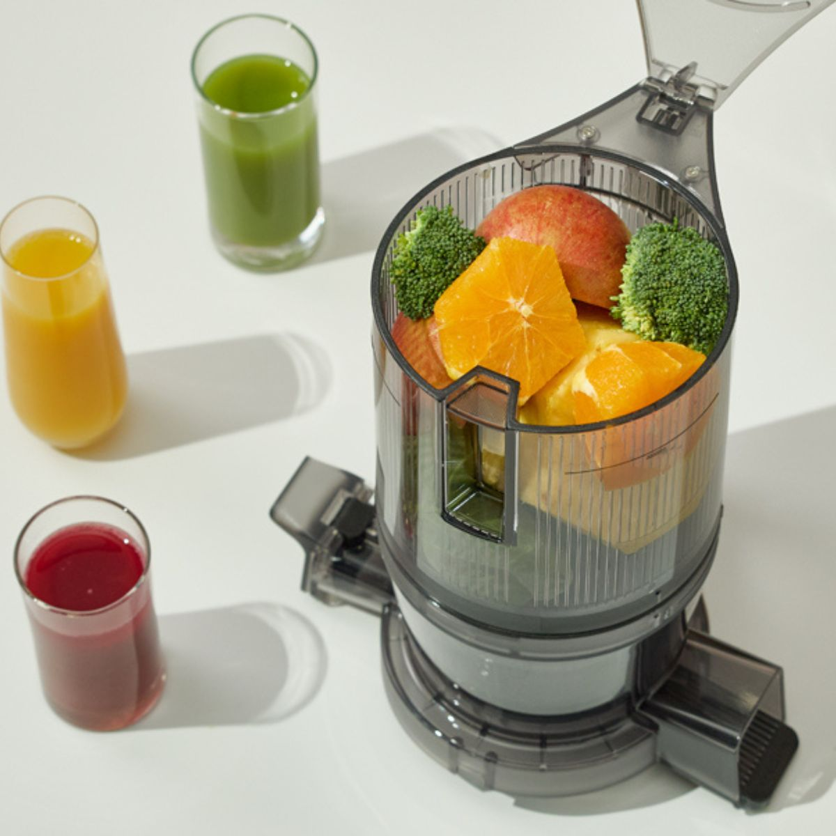 Ein Entsafter gefüllt mit Obst und Gemüse, daneben stehen drei Gläser Saft.