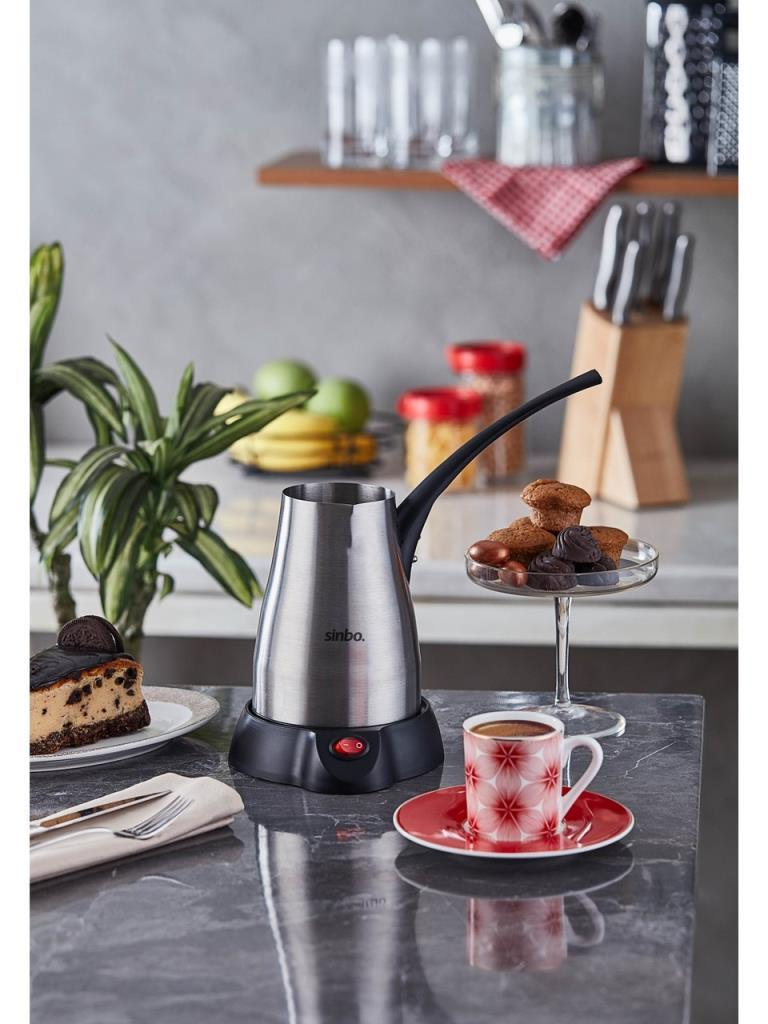 Mutfak tezgahında bir fincan kahve, kek ve muffin ile paslanmaz çelik elektrikli kahve cezvesi.