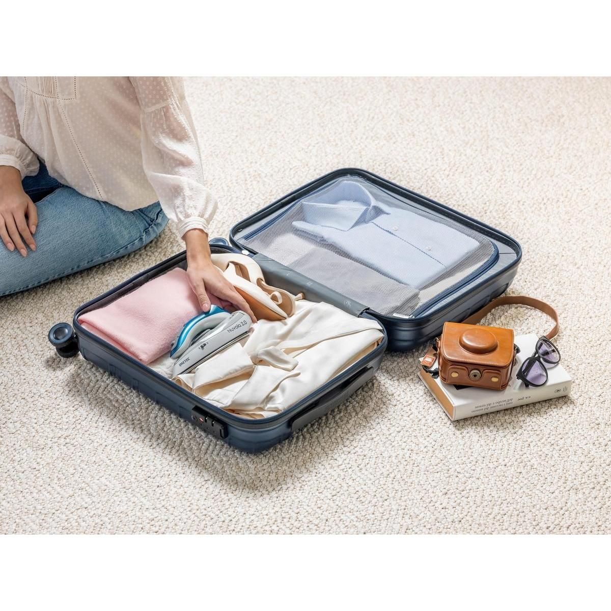 Una persona empaca una maleta azul colocando una mini plancha junto a la ropa.