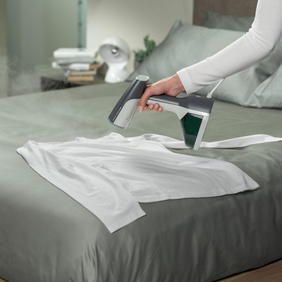 Una persona usa un vaporizzatore grigio su una camicia bianca su un letto.
