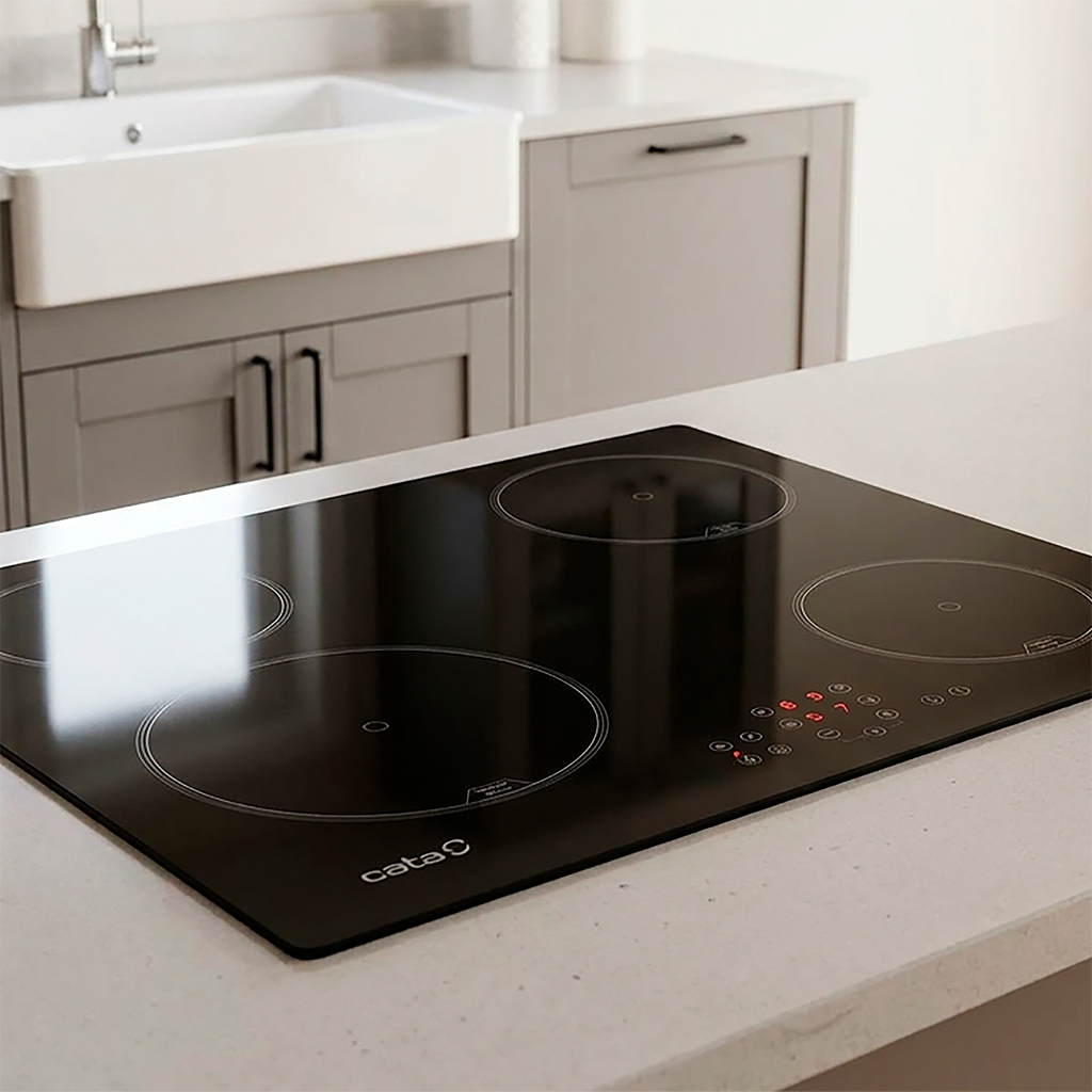 Placa de inducción negra en una isla de cocina blanca con fregadero y armarios grises al fondo.