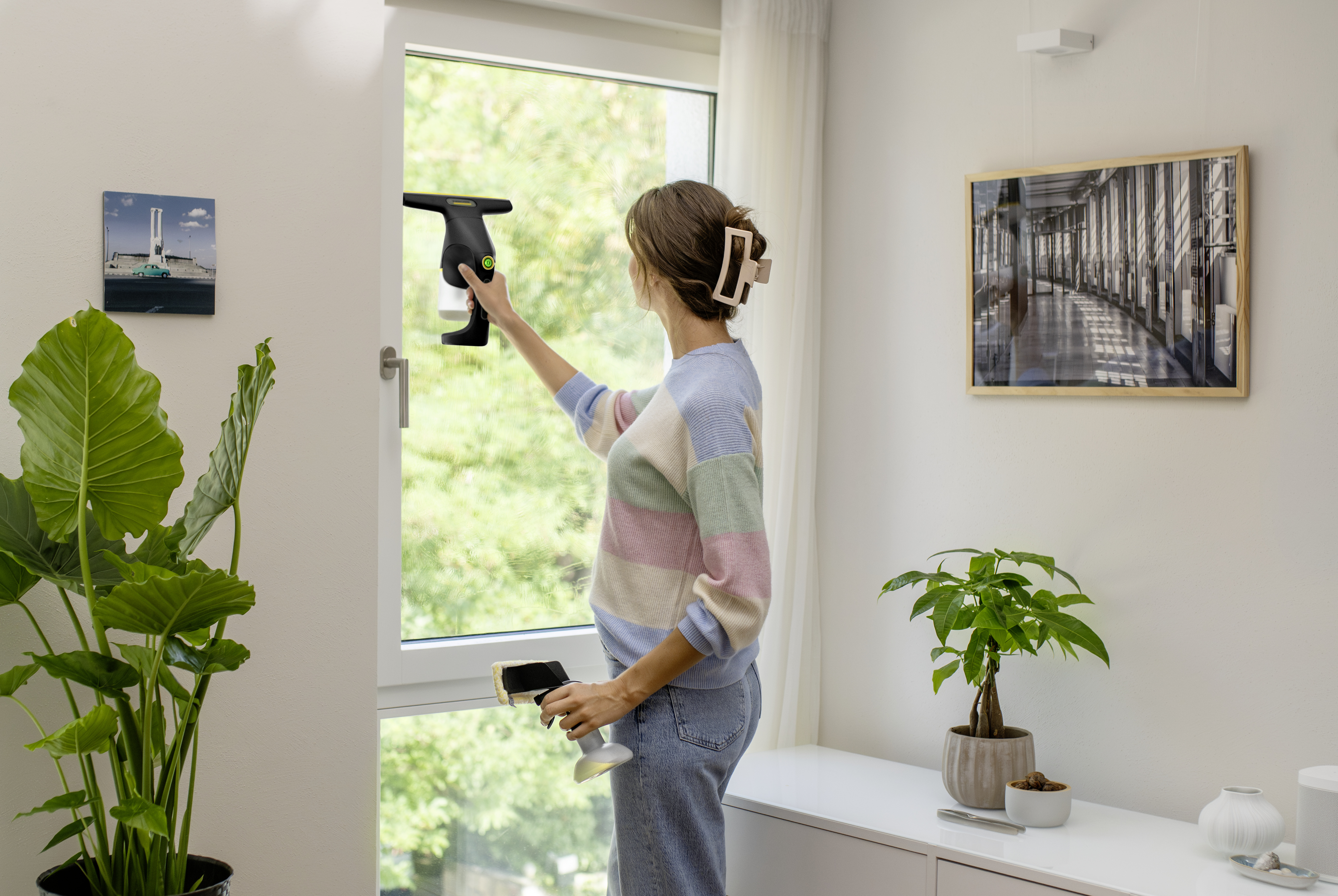 Eine Frau in einem Pastellpullover reinigt ein helles Fenster mit einem Fenstersauger.