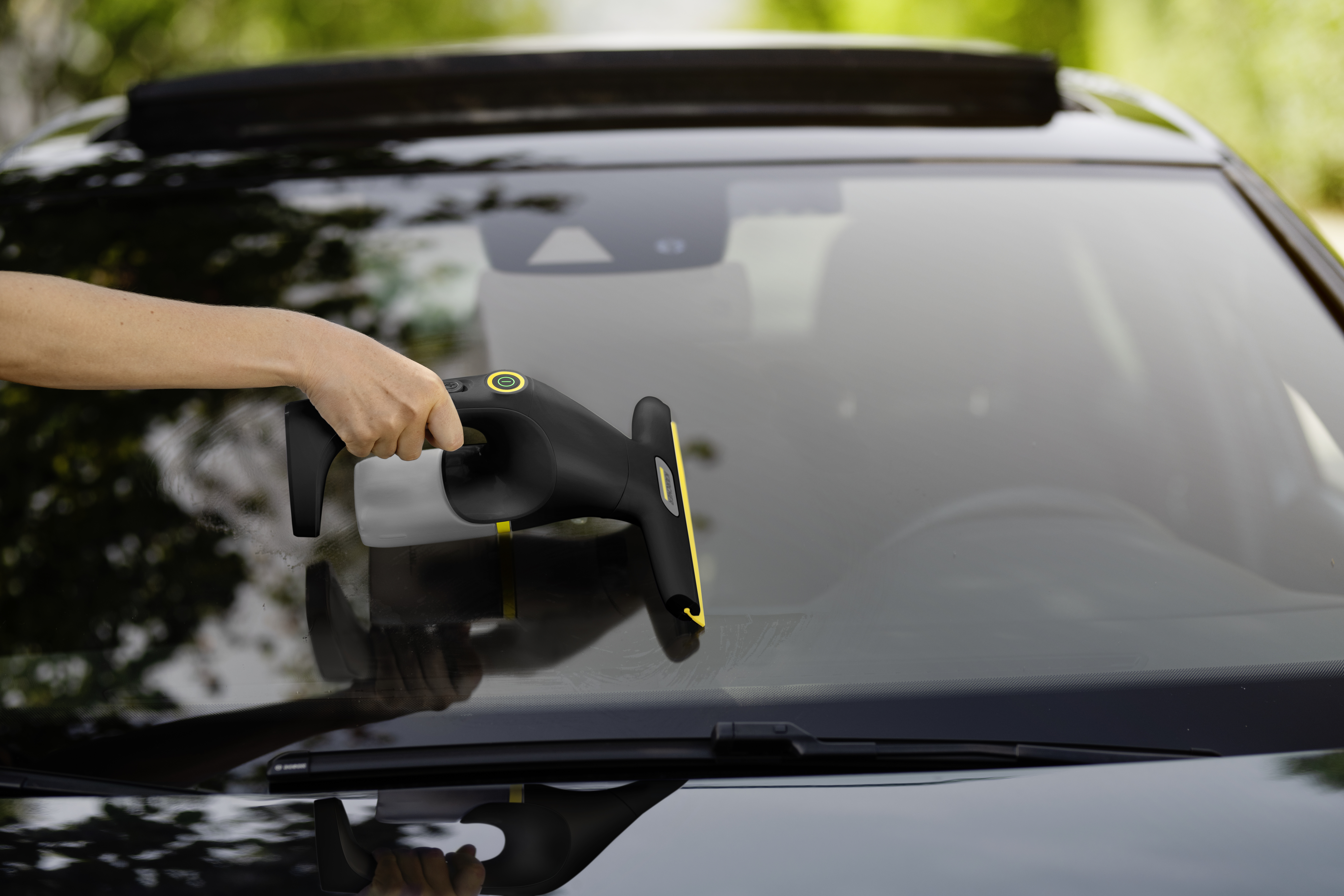 Eine Person reinigt die Windschutzscheibe eines schwarzen Autos mit einem gelb-schwarzen Fenstersauger.