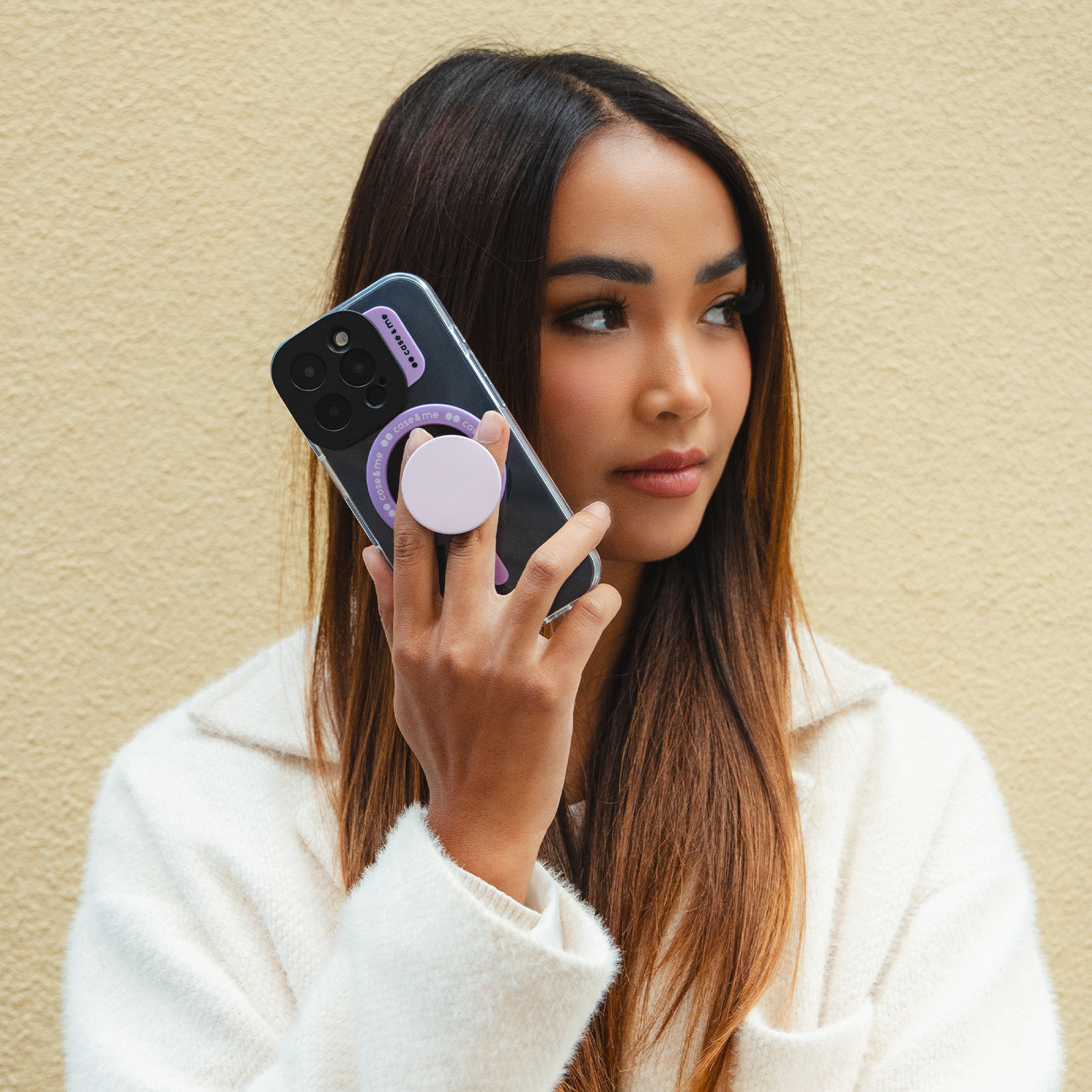 Una mujer con cabello castaño largo y abrigo blanco sostiene un teléfono con agarre morado.