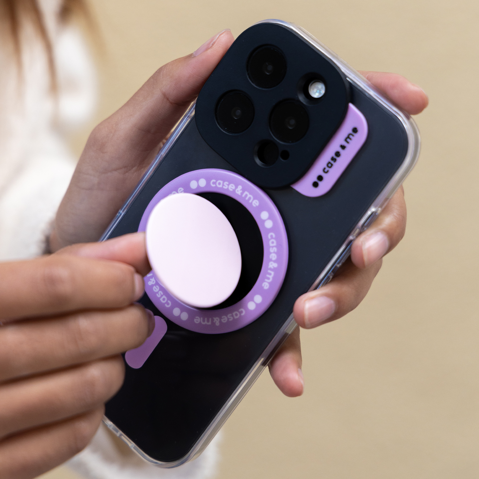 Una mano sostiene un teléfono inteligente negro con un soporte redondo morado en la parte posterior.