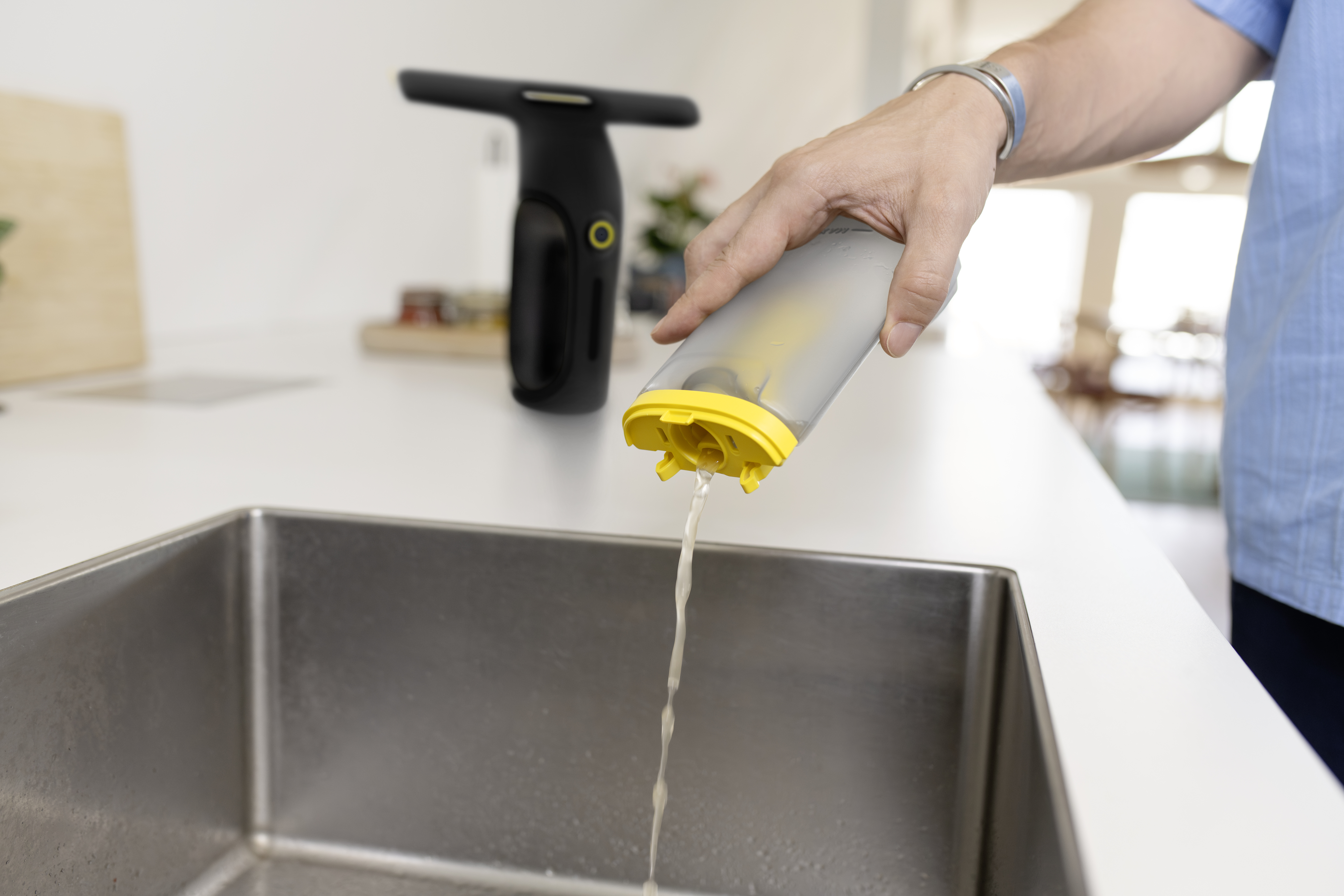 Eine Person gießt schmutziges Wasser aus einem Behälter mit gelbem Deckel in ein Waschbecken.