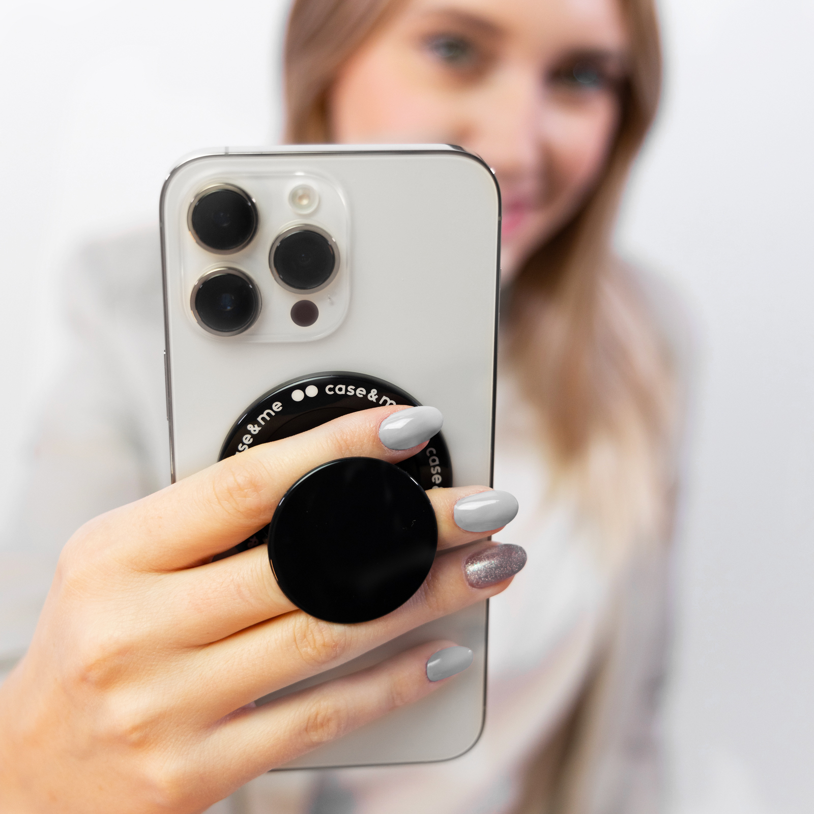 Una mujer sostiene un smartphone con un soporte negro en la parte trasera, mostrando sus uñas grises.