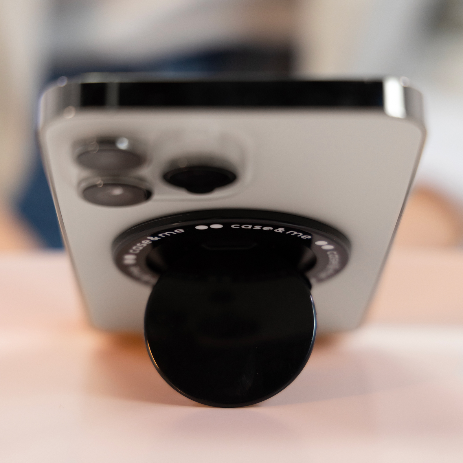 Parte trasera de un smartphone blanco sobre una mesa, con tres lentes de cámara y un soporte negro redondo.