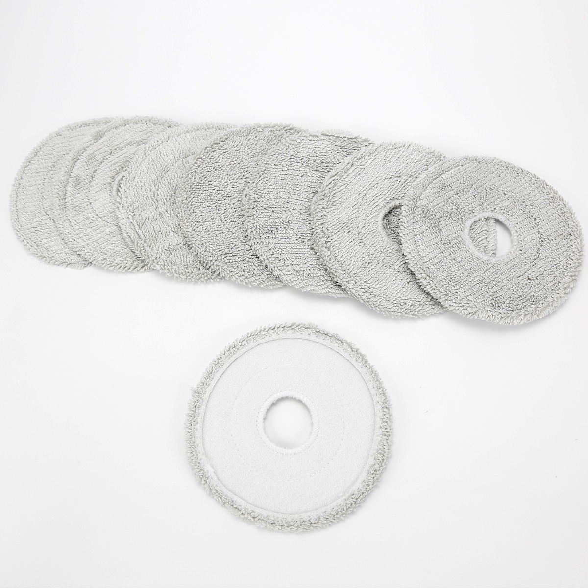 Eine Reihe grauer, runder Wischmopp-Pads mit Loch und ein einzelnes Pad darunter auf weißem Grund.