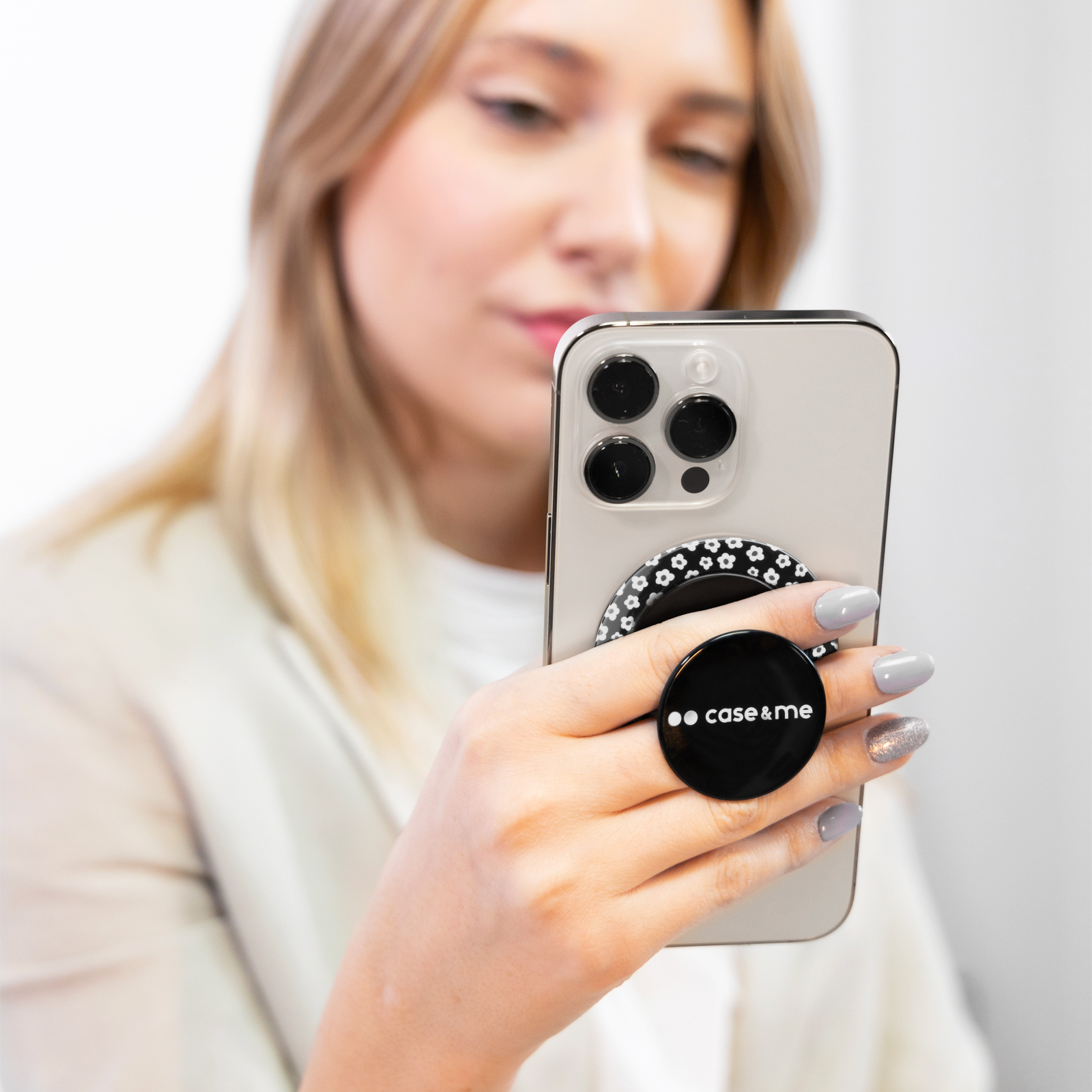 Una mujer sostiene un teléfono con un soporte negro y blanco con el logotipo case & me.