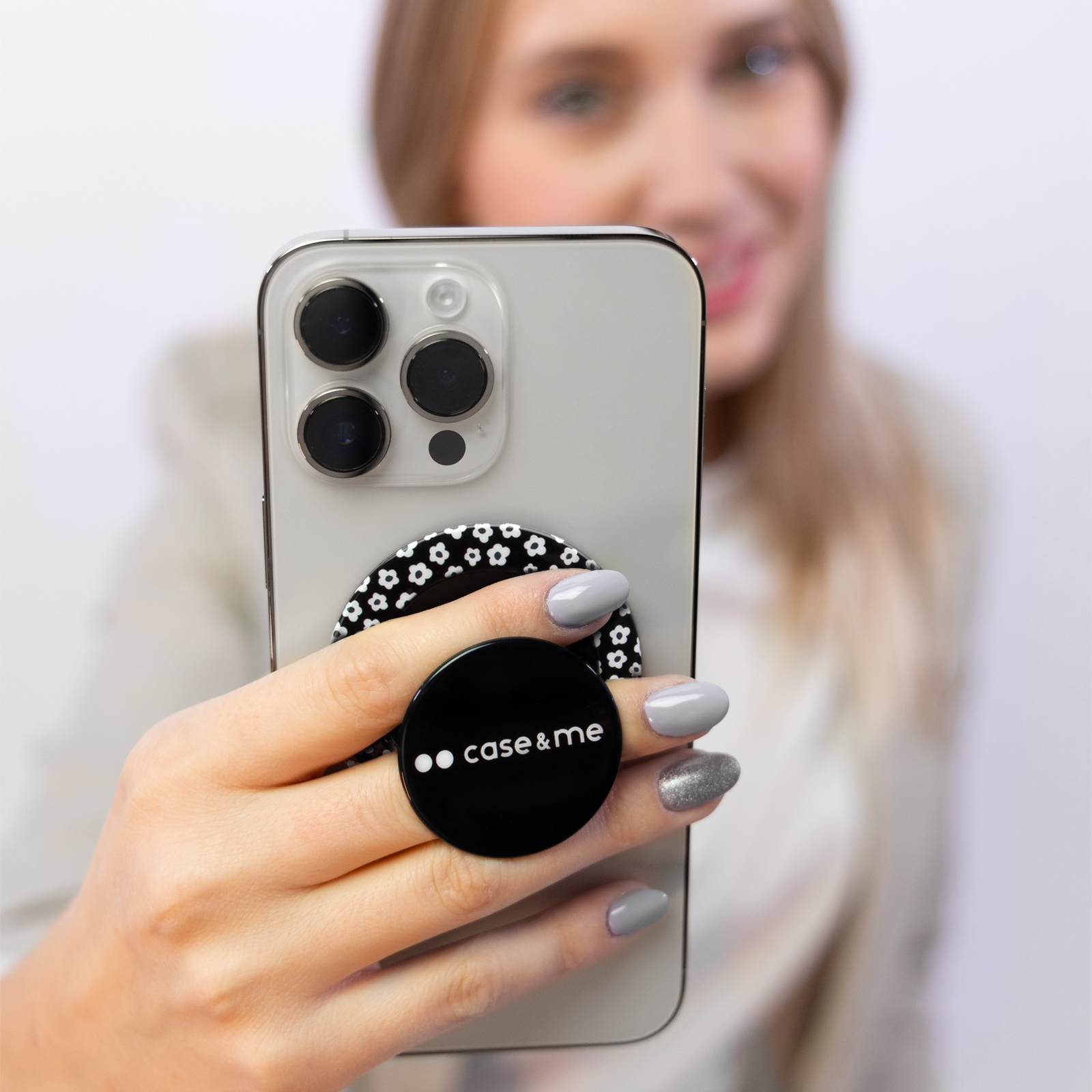 Una mujer sostiene un smartphone con un soporte negro redondo con patrón floral blanco en la parte trasera.