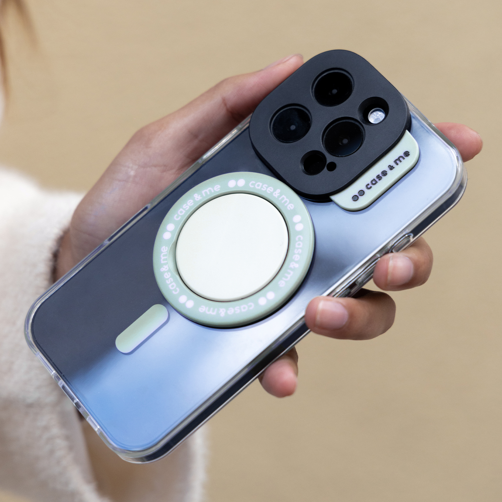 Una mano sostiene un smartphone con funda transparente, anillo magnético y protector.