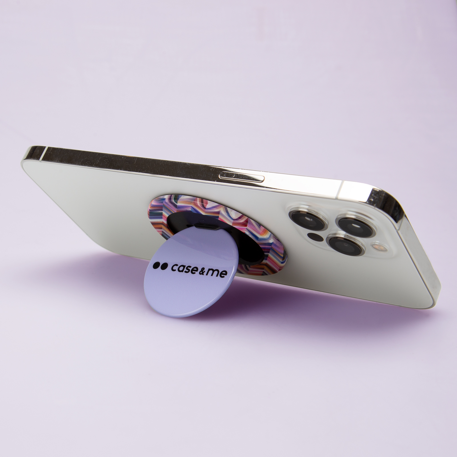 Un teléfono inteligente con un soporte redondo morado con la marca case&me sobre una superficie morada clara.