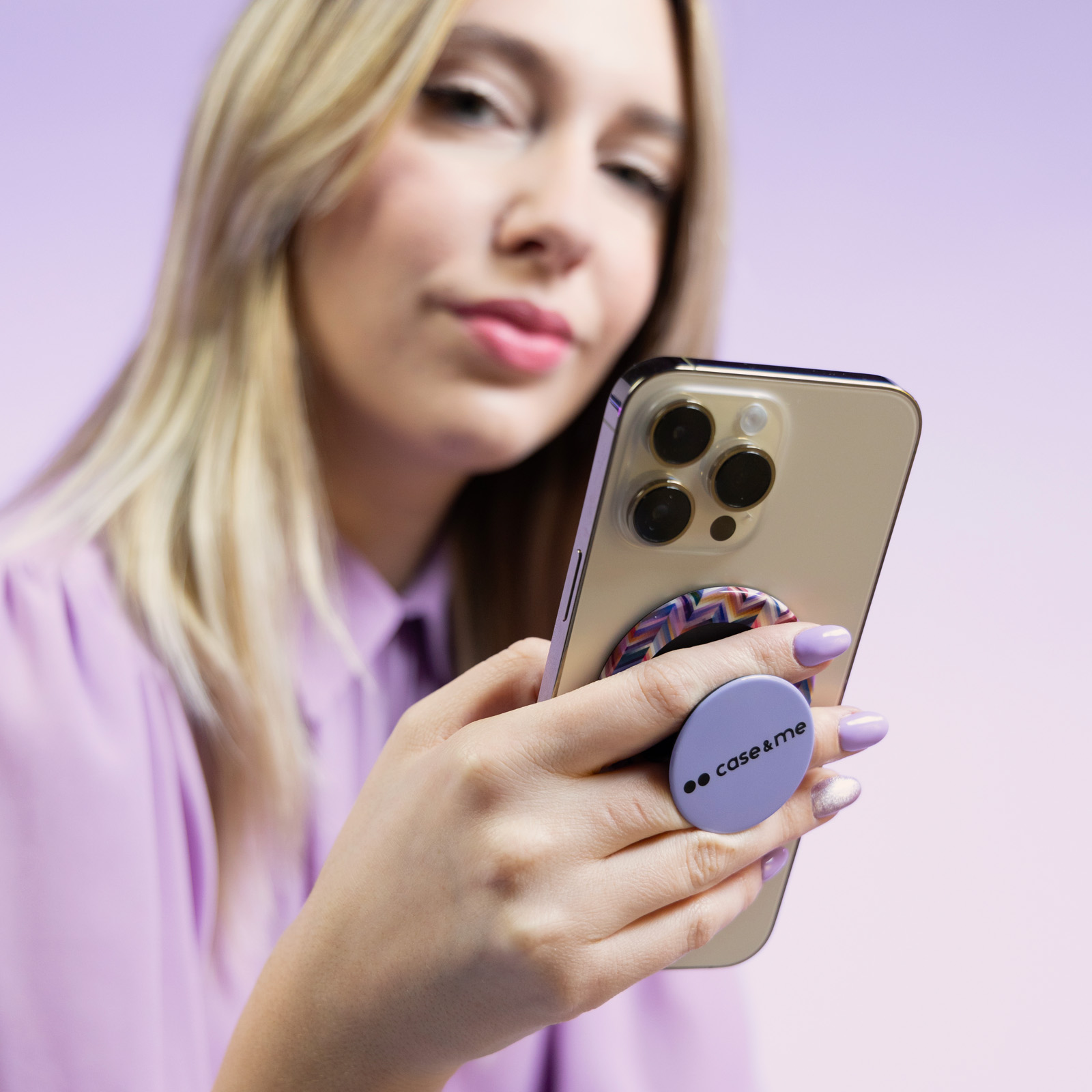 Una mujer rubia sostiene un smartphone con un soporte morado sobre un fondo morado.