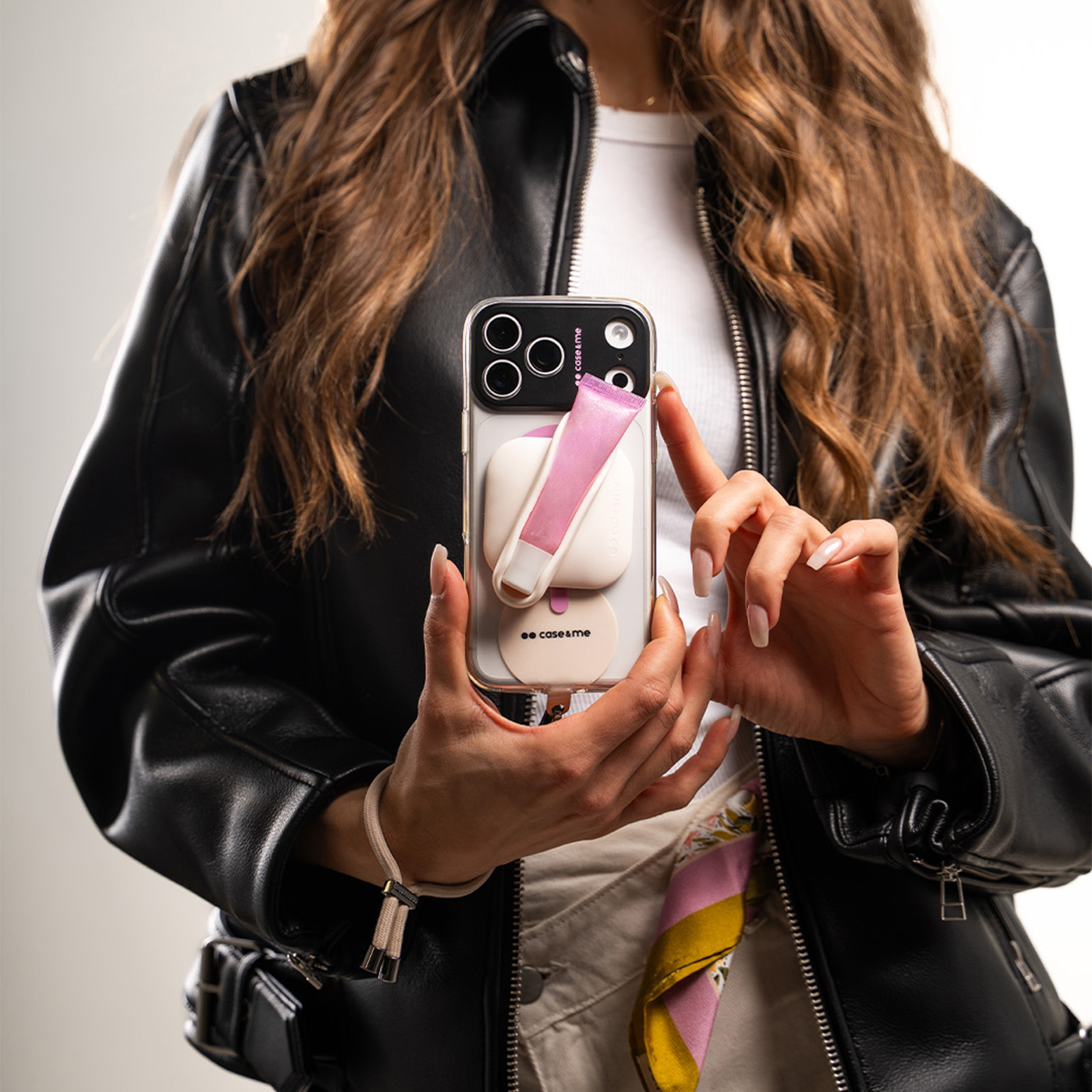 Una donna con una giacca di pelle nera tiene uno smartphone con lucidalabbra rosa e accessori sul retro.
