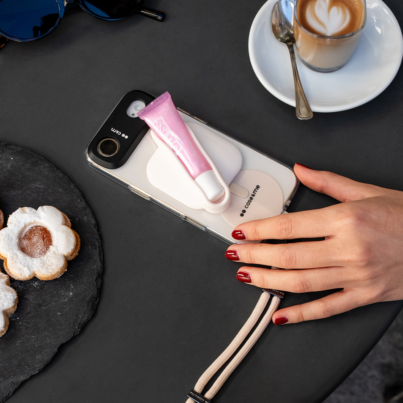 Telefono con lucidalabbra, caffè e biscotti su un tavolo nero.