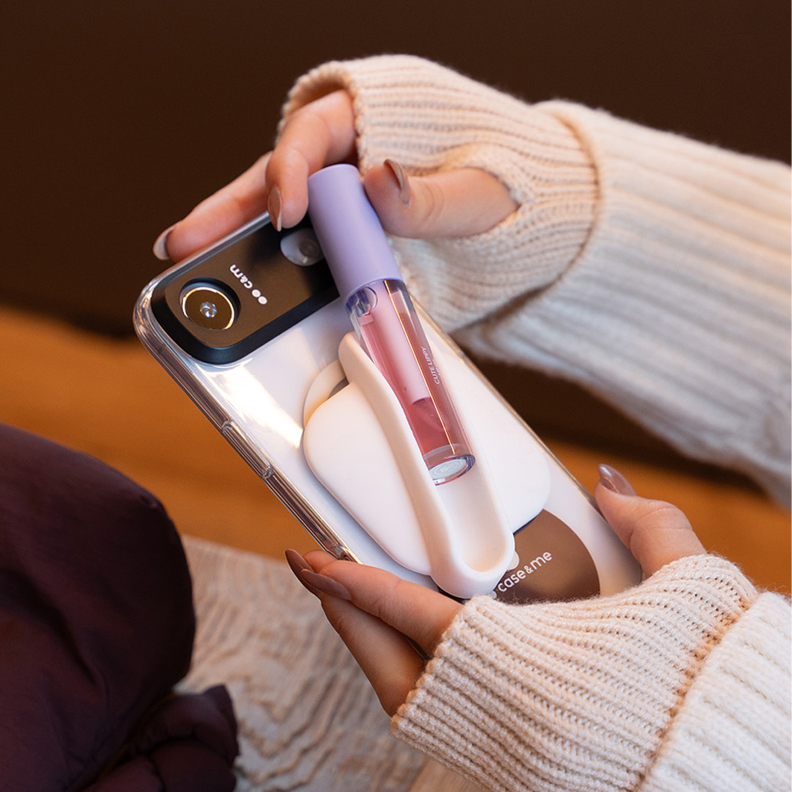 Persona con maglione bianco tiene uno smartphone con rossetto nel supporto.