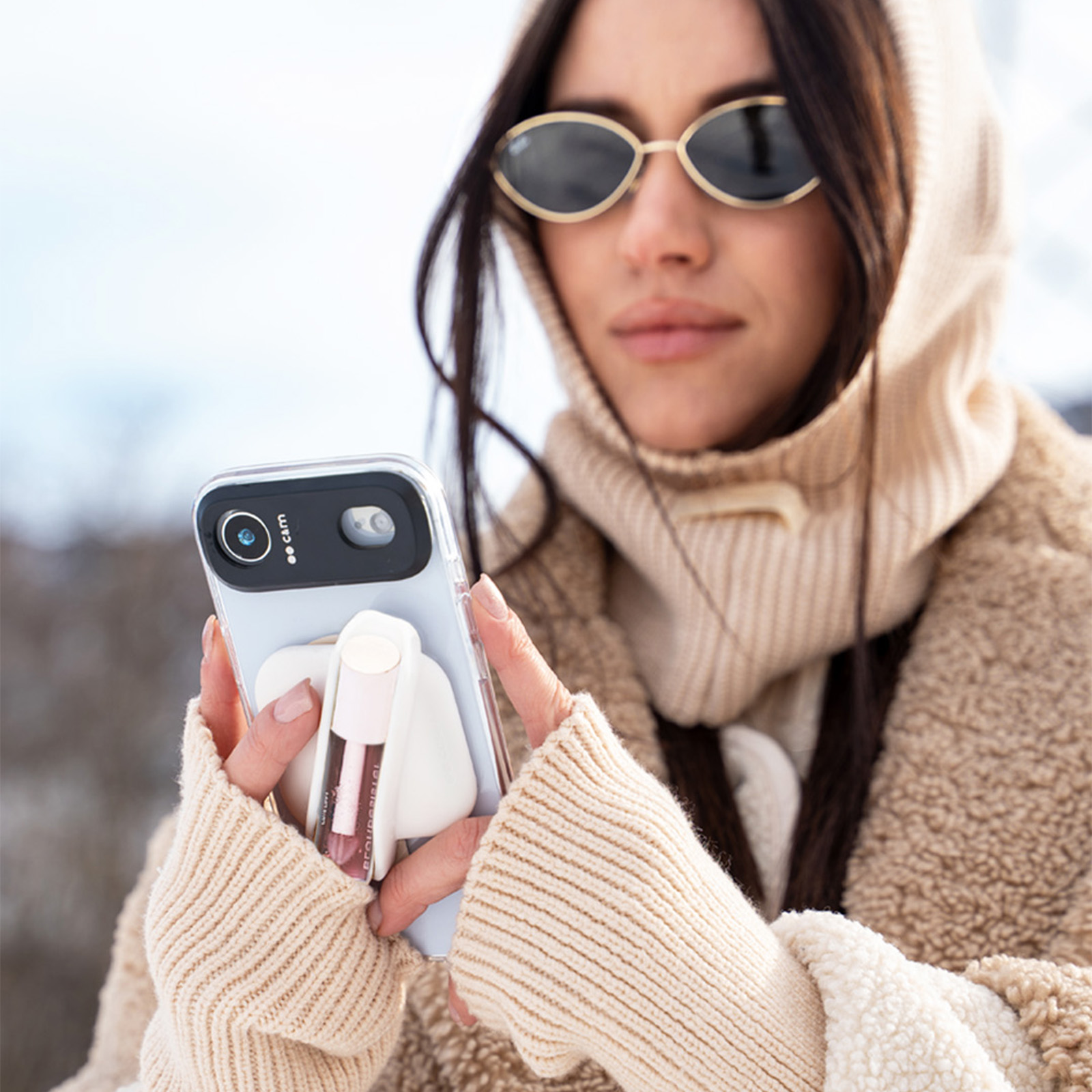 Una donna con felpa crema tiene un telefono con un lucidalabbra sul retro.