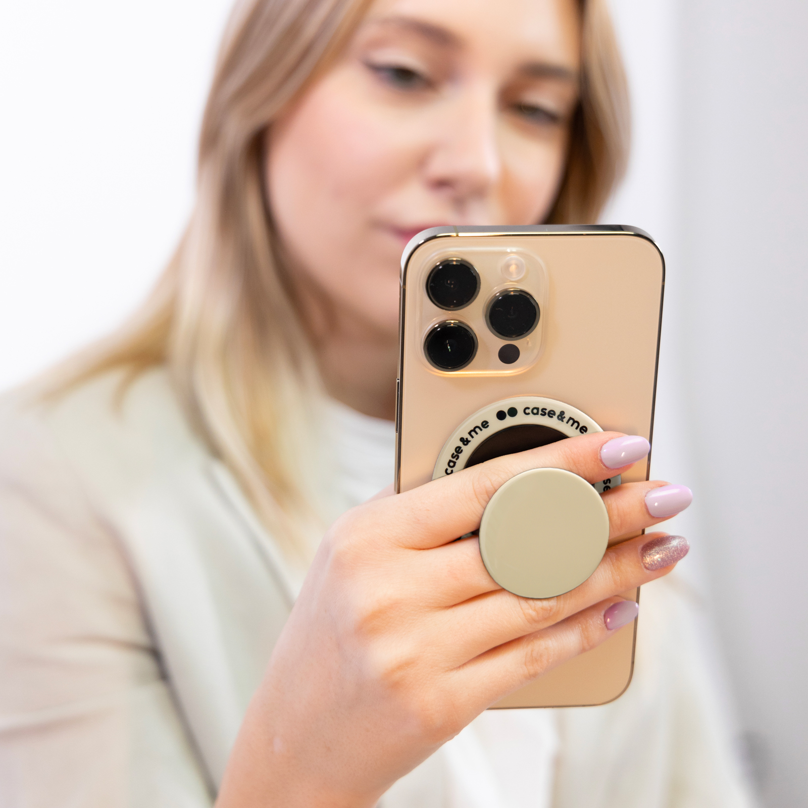 Una mujer rubia sostiene un teléfono inteligente dorado con un soporte circular en la parte posterior.
