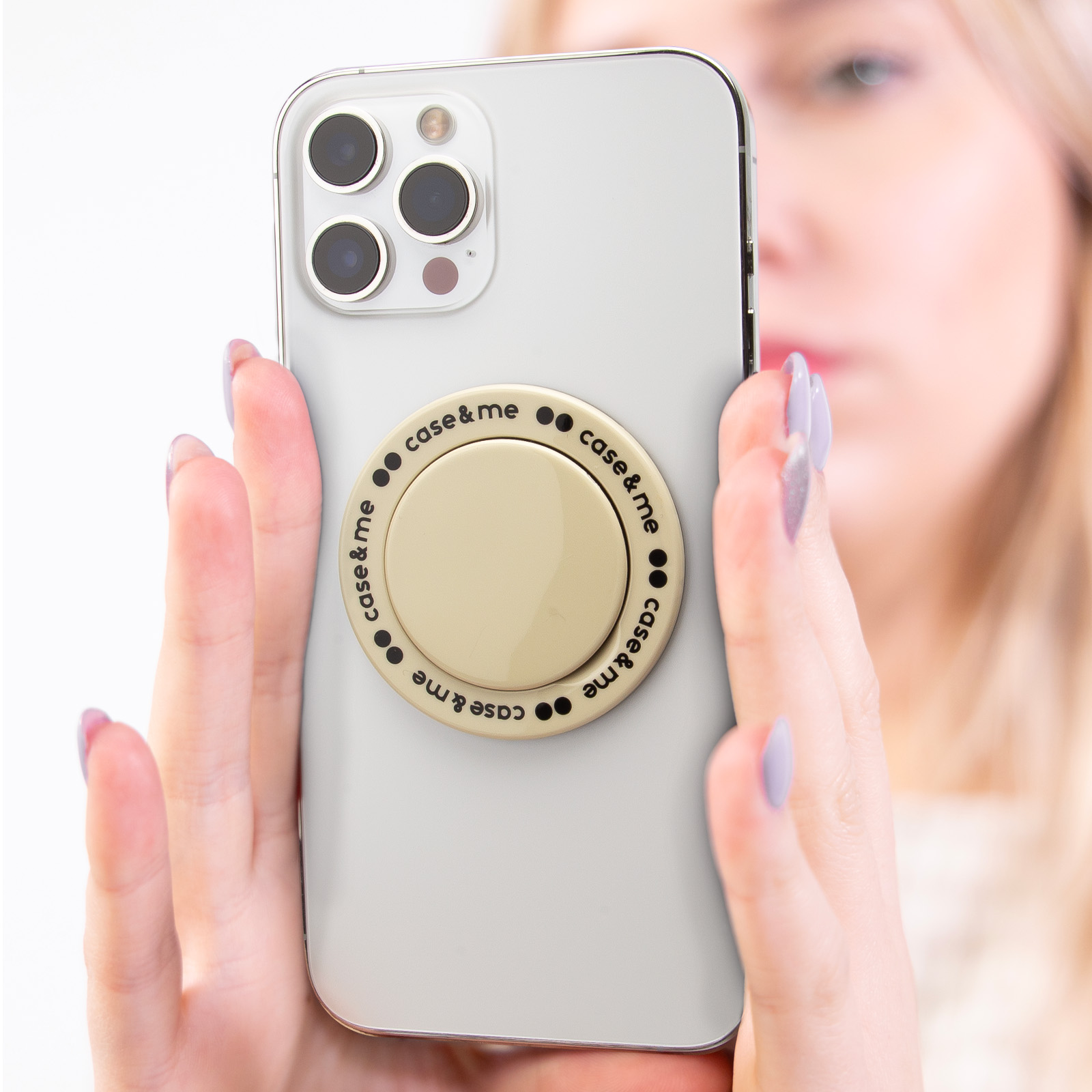 Una mujer sostiene un teléfono con un soporte redondo beige y texto case & me.
