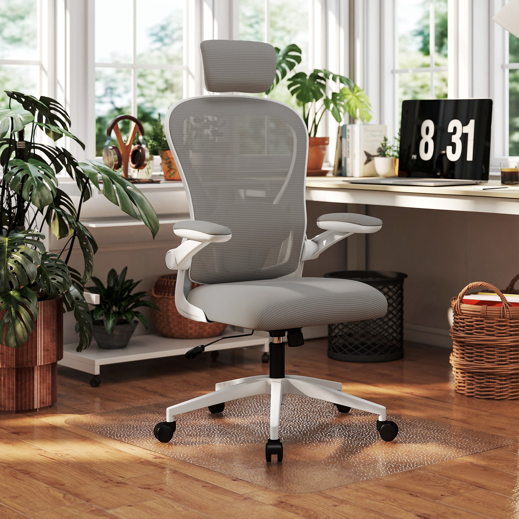 Una silla de oficina de malla gris con marco y reposacabezas blancos en una oficina en casa luminosa y con plantas.