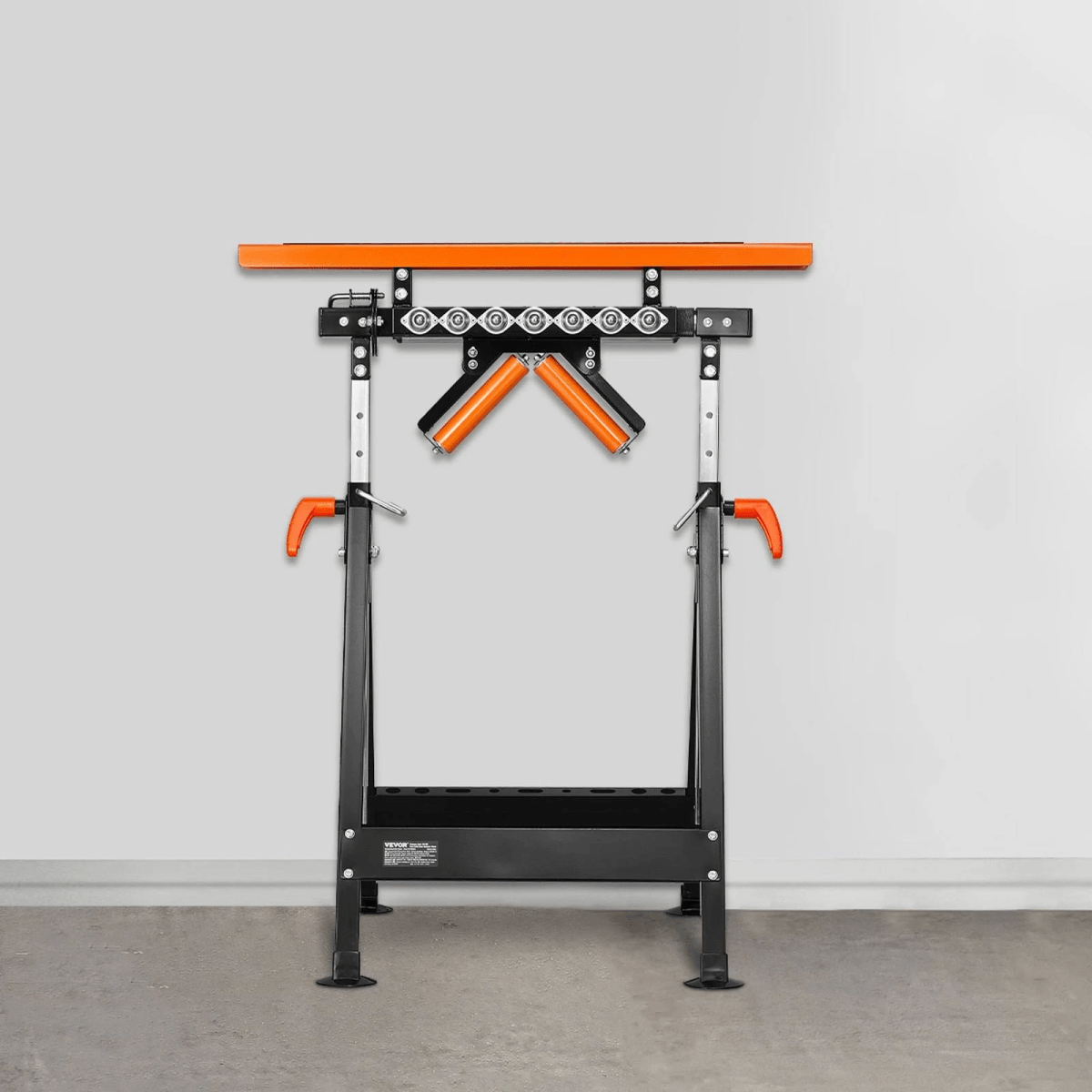Un soporte de taller negro con detalles naranjas y una pista de rodillos superior contra una pared gris.