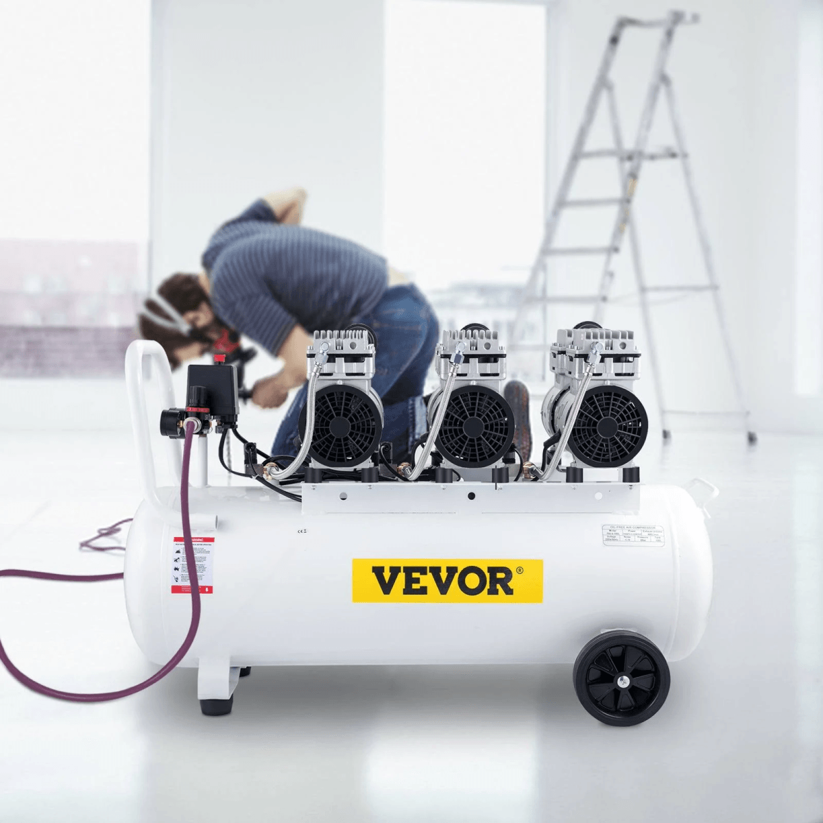 Un compresor de aire VEVOR blanco con tres motores se encuentra en una habitación luminosa, con un trabajador y una escalera.
