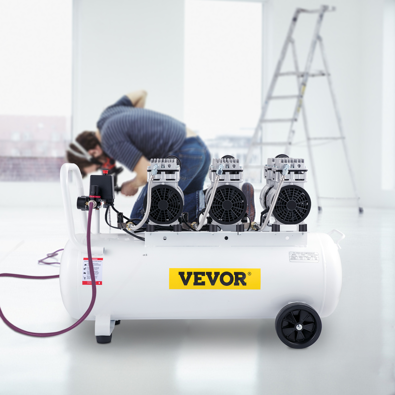 Un compresor VEVOR blanco con tres motores en primer plano y un trabajador trabajando en el fondo desenfocado.
