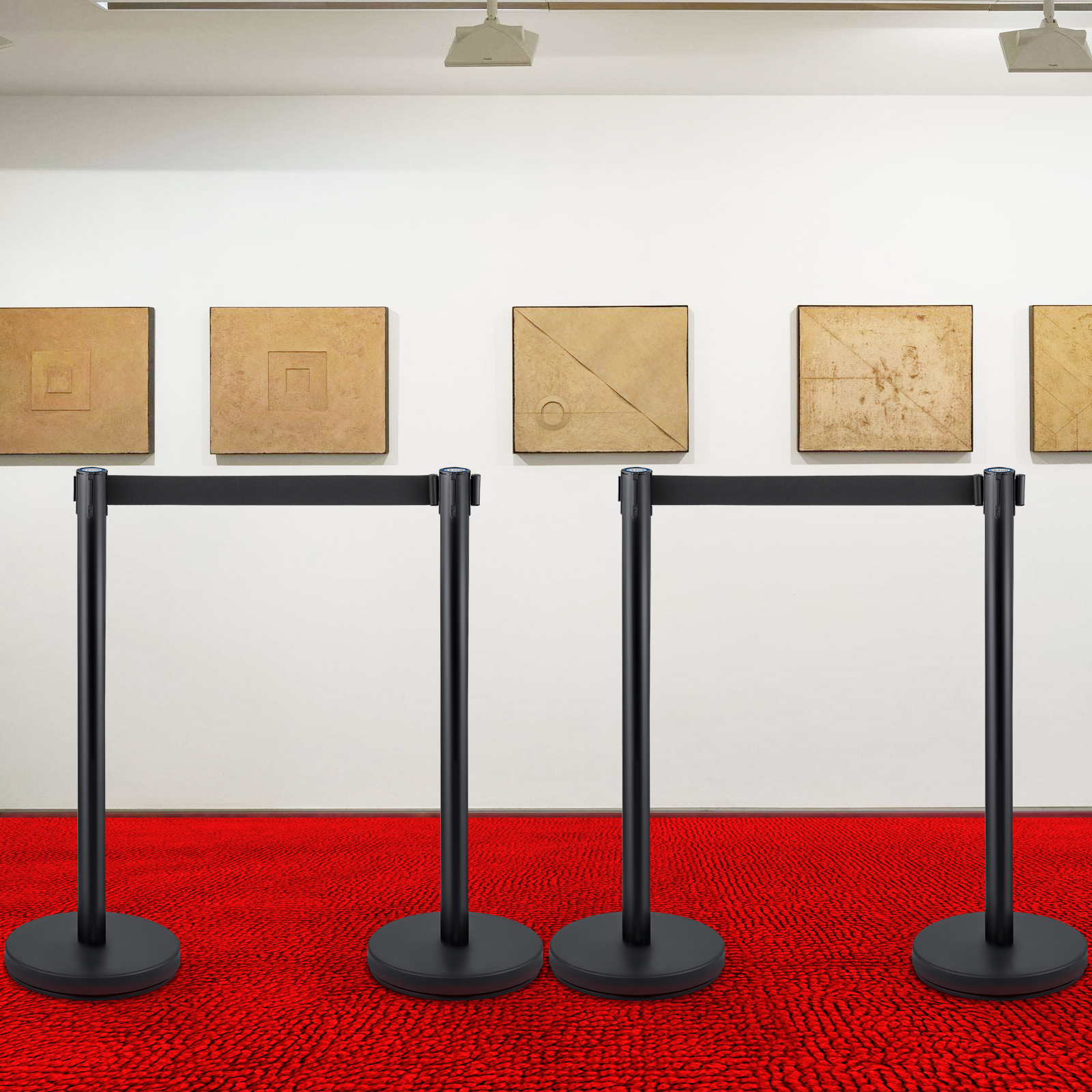 Postes negros con cintas se encuentran sobre una alfombra roja frente a una pared de galería con arte.
