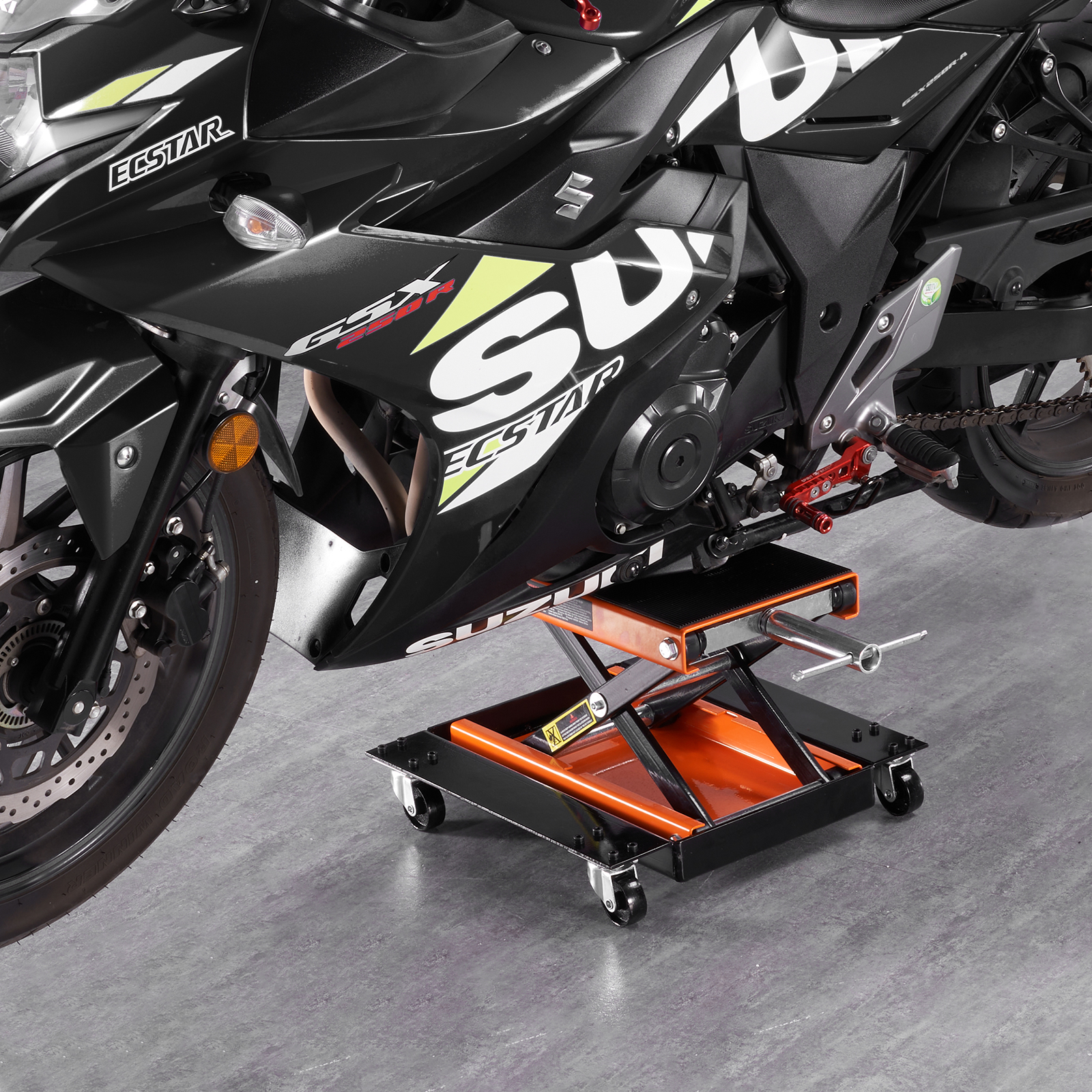 Una motocicleta Suzuki negra apoyada en un elevador con ruedas naranja y negro sobre un suelo gris.