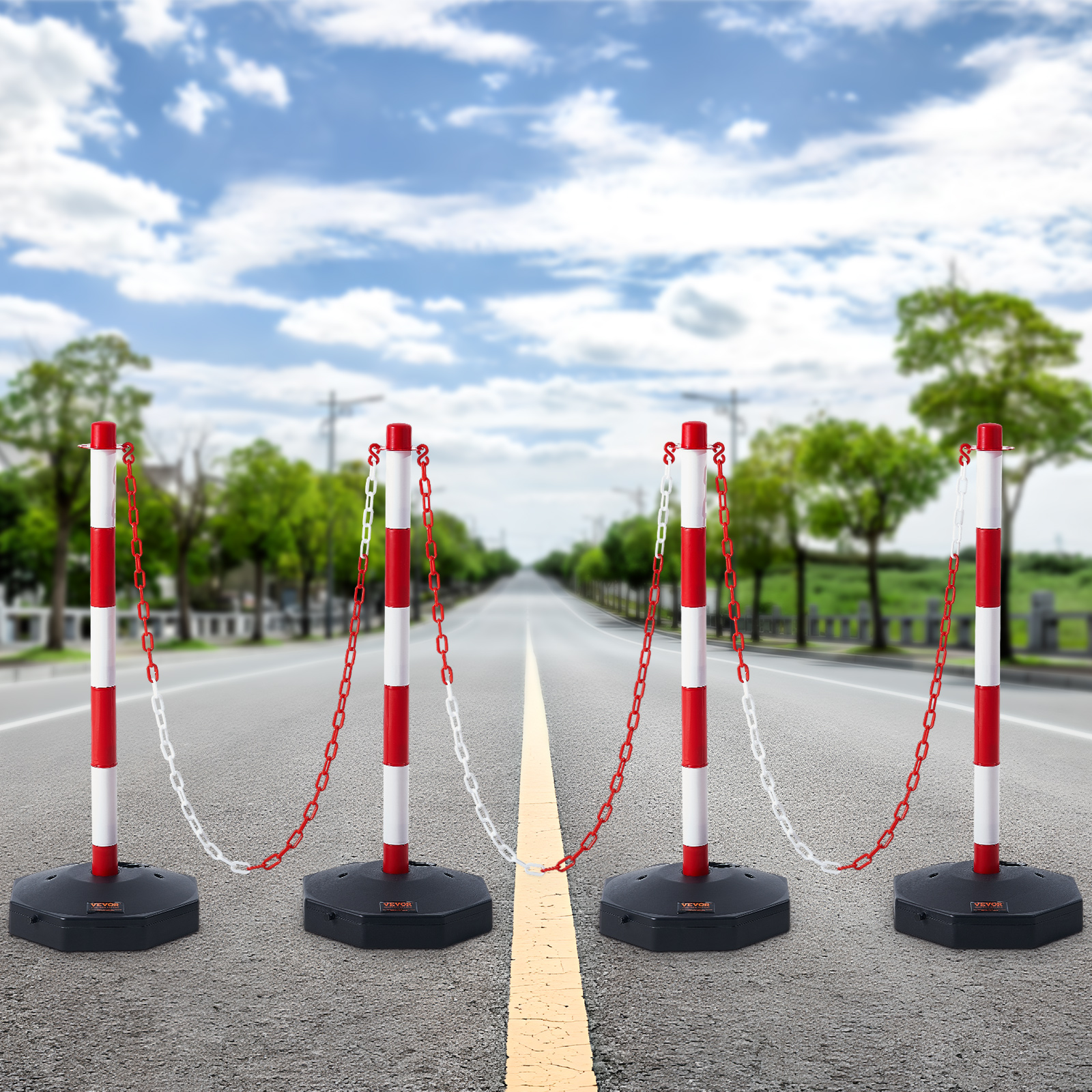 Cuatro postes rojos y blancos con cadenas bloquean una carretera vacía bajo un cielo azul.