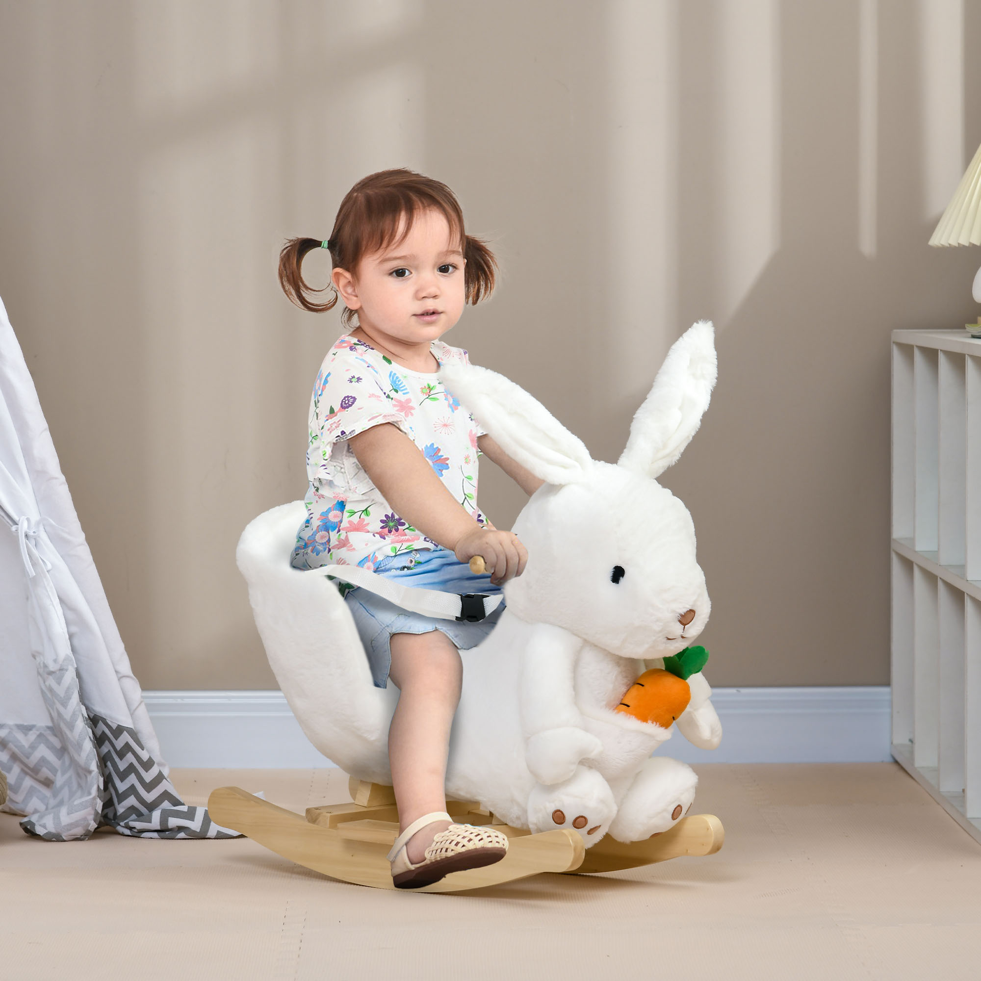 Una bambina con le codine cavalca un coniglio a dondolo di peluche bianco in una stanza.