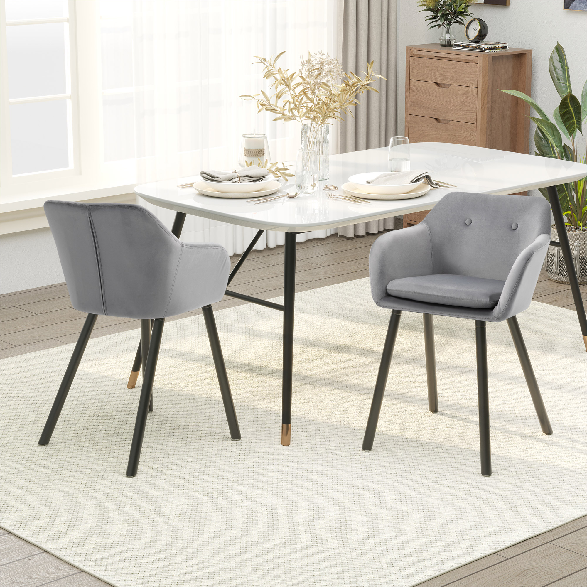 Sala da pranzo con tavolo bianco, due poltroncine grigie, stoviglie e tappeto chiaro davanti a una finestra.