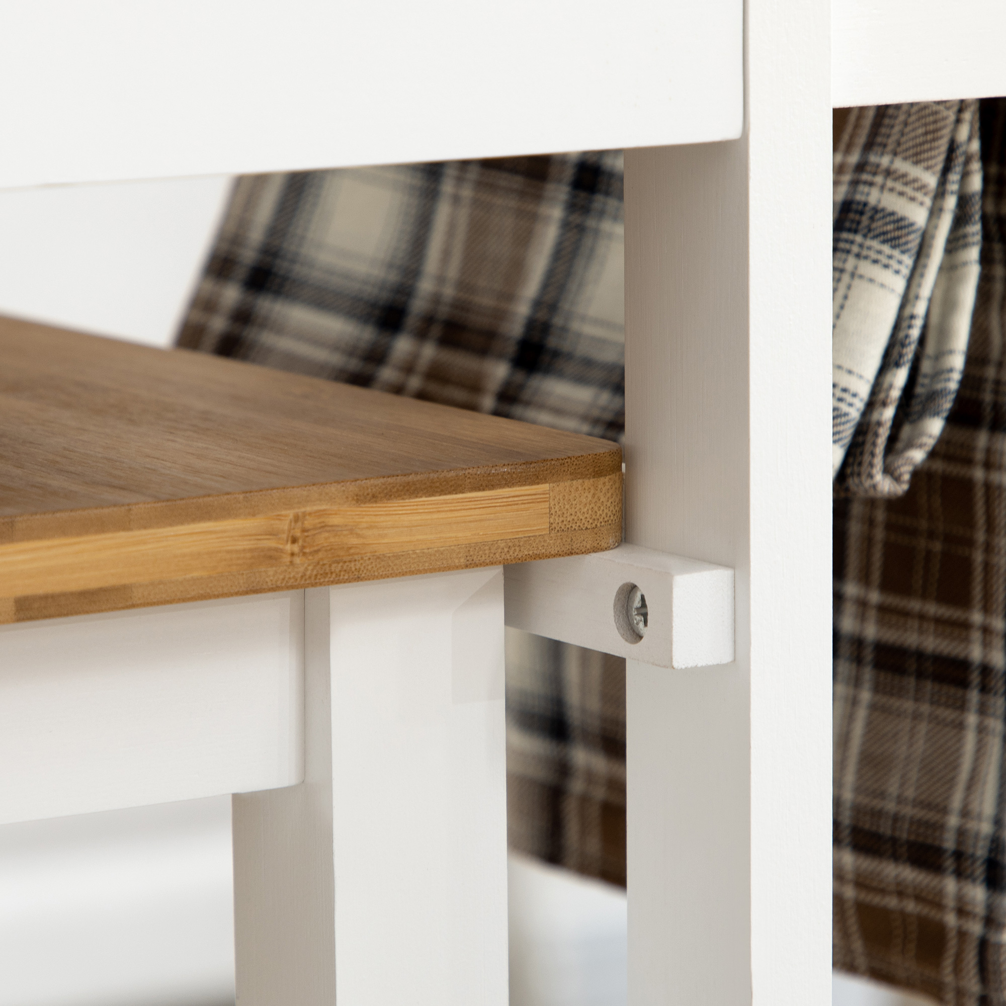 Primer plano de una mesa de madera blanca con tablero de madera marrón y tela a cuadros al fondo.