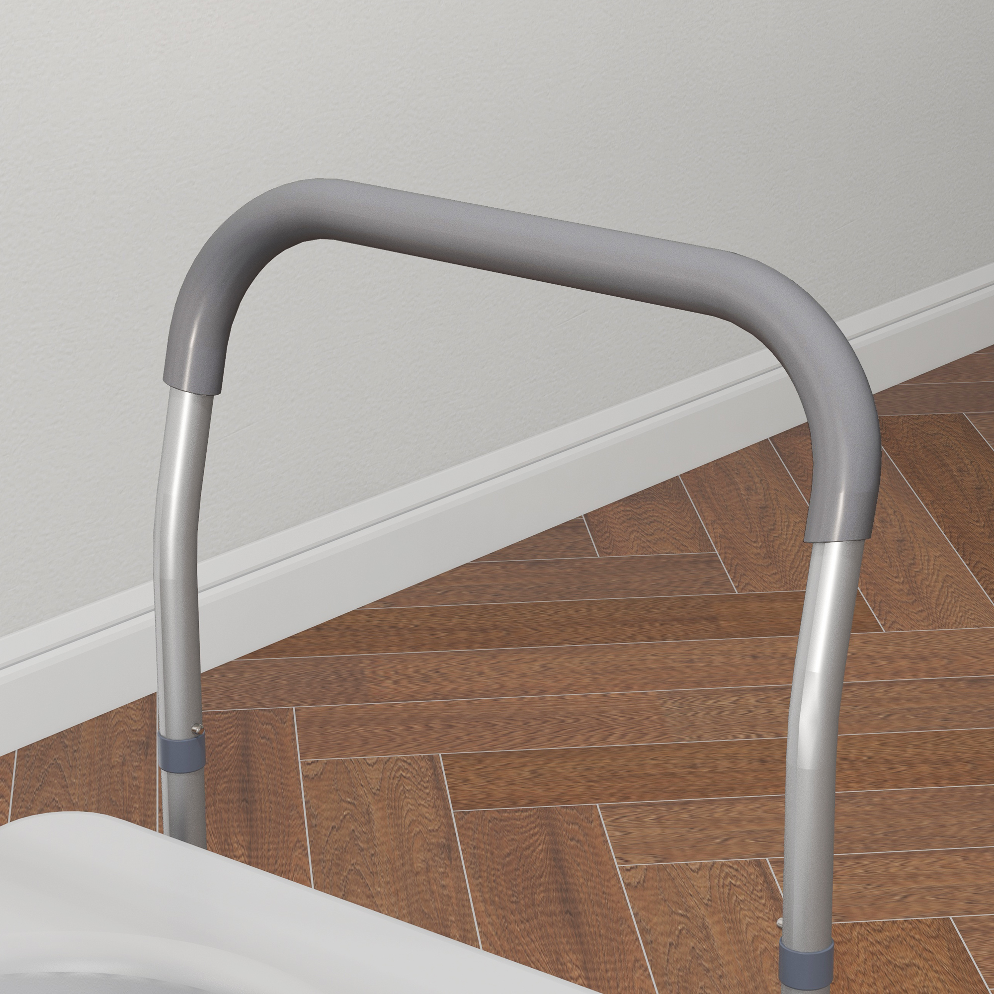 Una barra de seguridad gris con patas de aluminio para el inodoro, colocada ante una pared blanca y suelo de parquet.