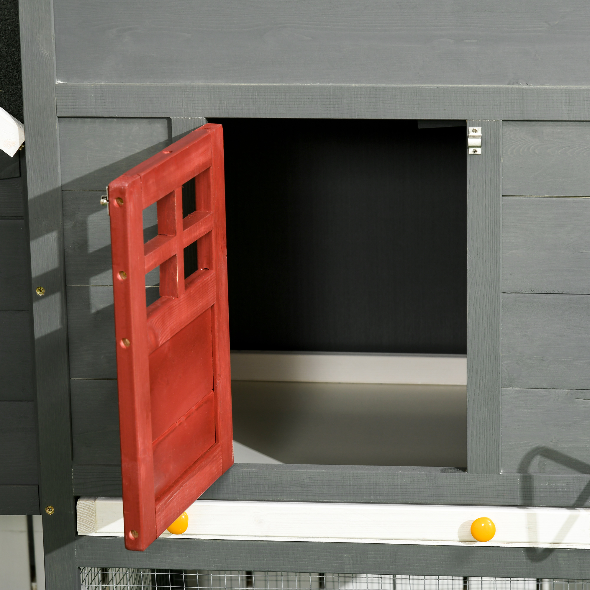 Un recinto de madera gris con una puerta roja de madera entreabierta que muestra un interior luminoso.