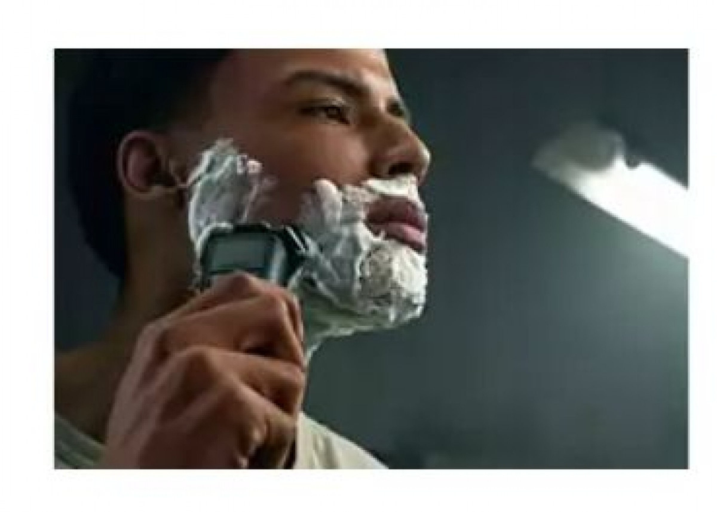Un uomo che si rade il viso con un rasoio elettrico e schiuma da barba.