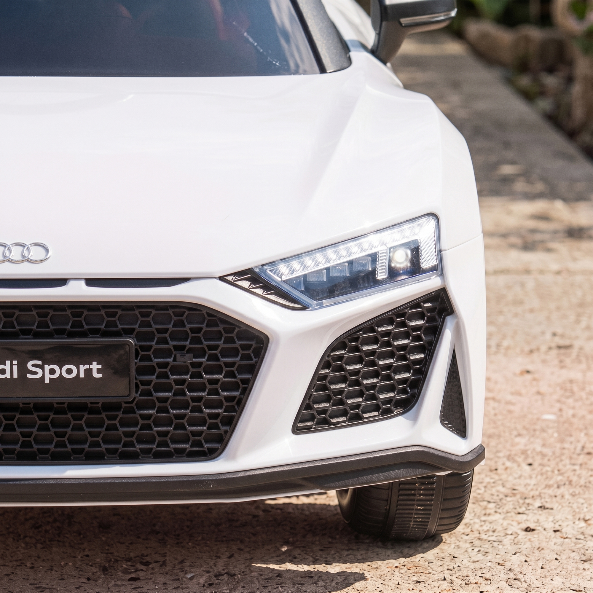 Primer plano del frontal de un coche de juguete Audi Sport blanco con faros iluminados.