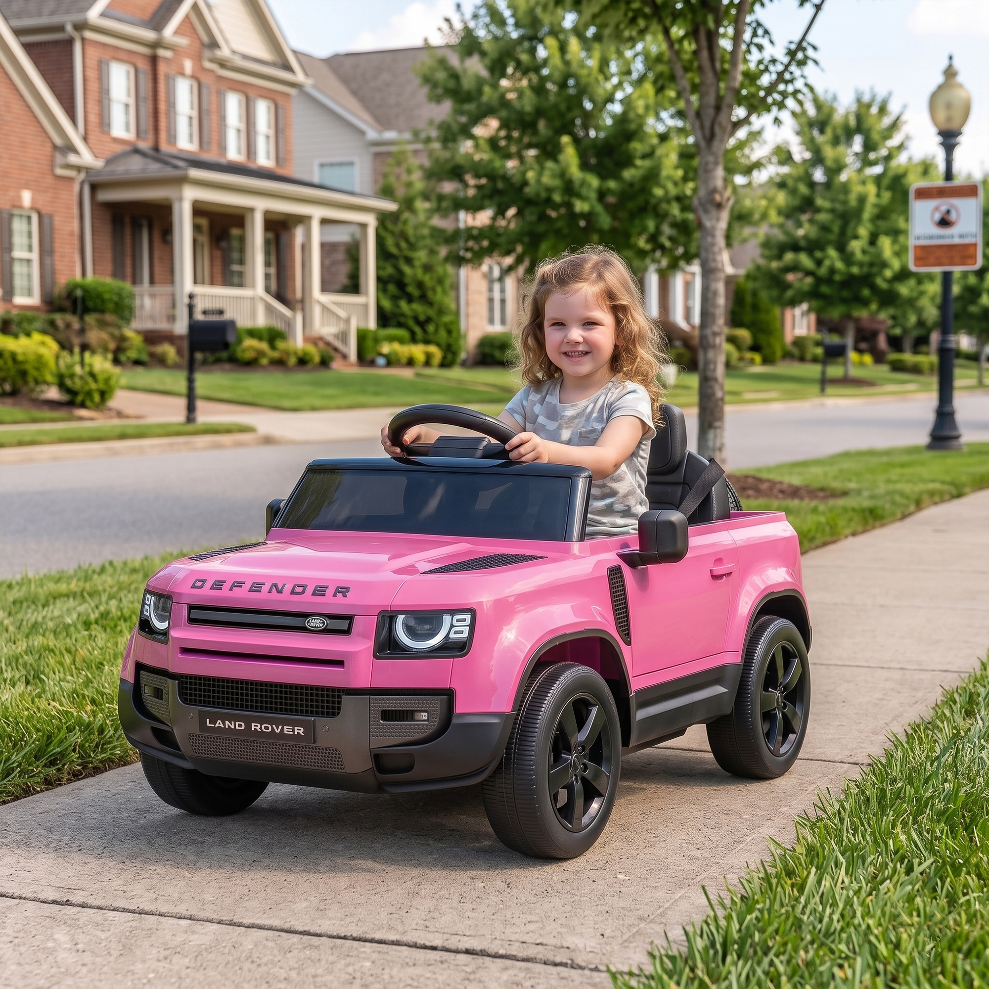 Una niña sonríe mientras conduce un Land Rover de juguete rosa en una acera.