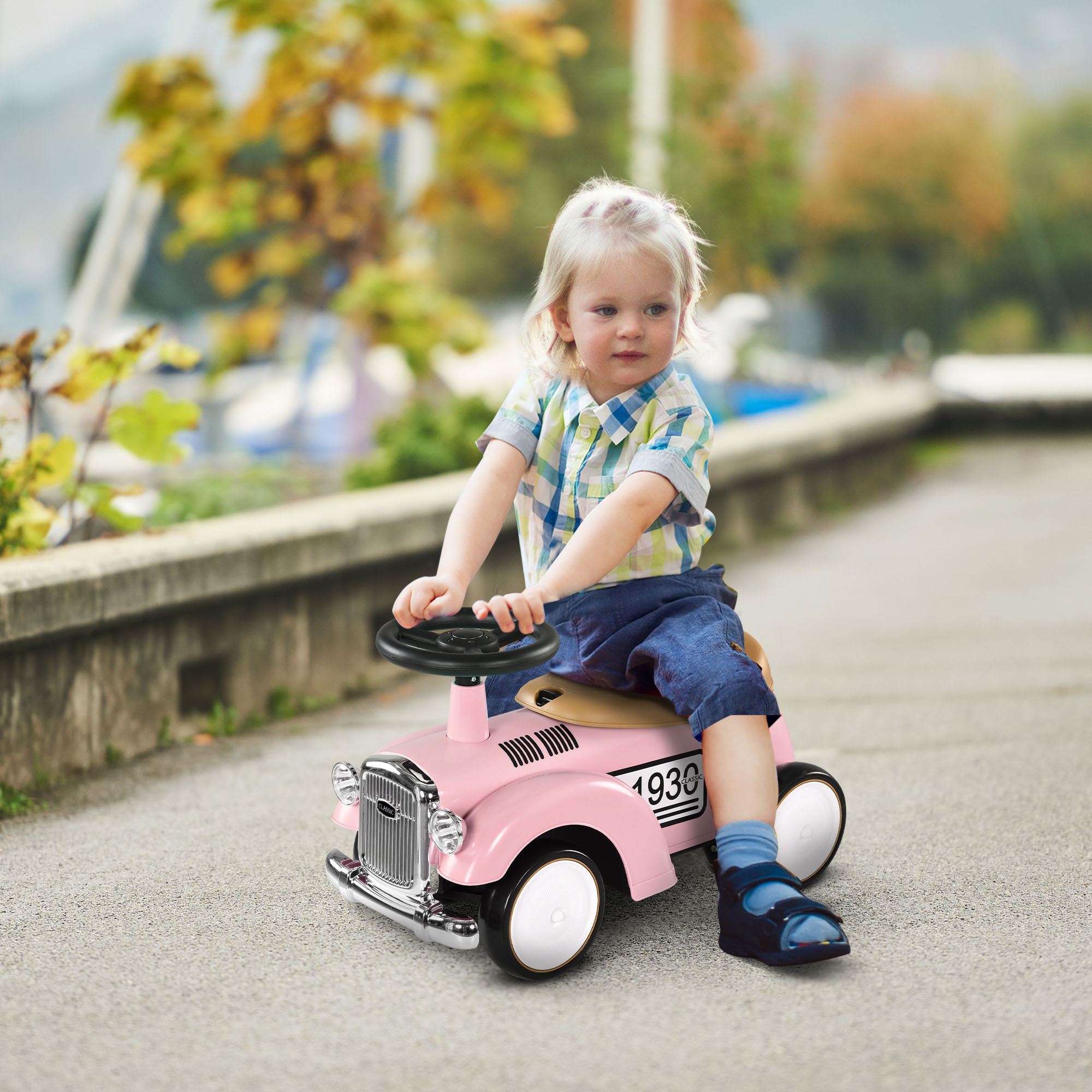 Un niño rubio con camisa a cuadros monta en un coche de juguete rosa por un camino pavimentado.