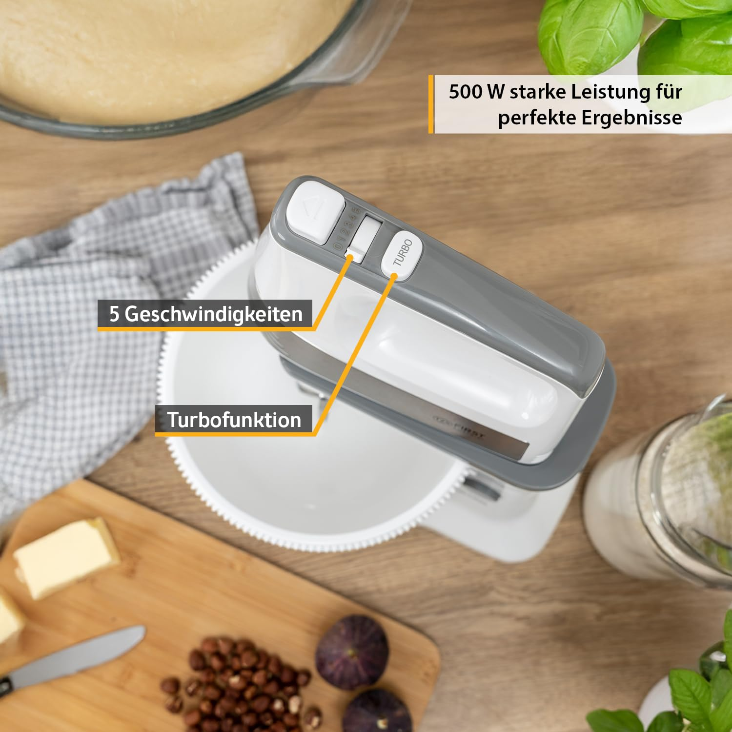 Un'impastatrice bianca e grigia su un piano di lavoro in legno con ingredienti.