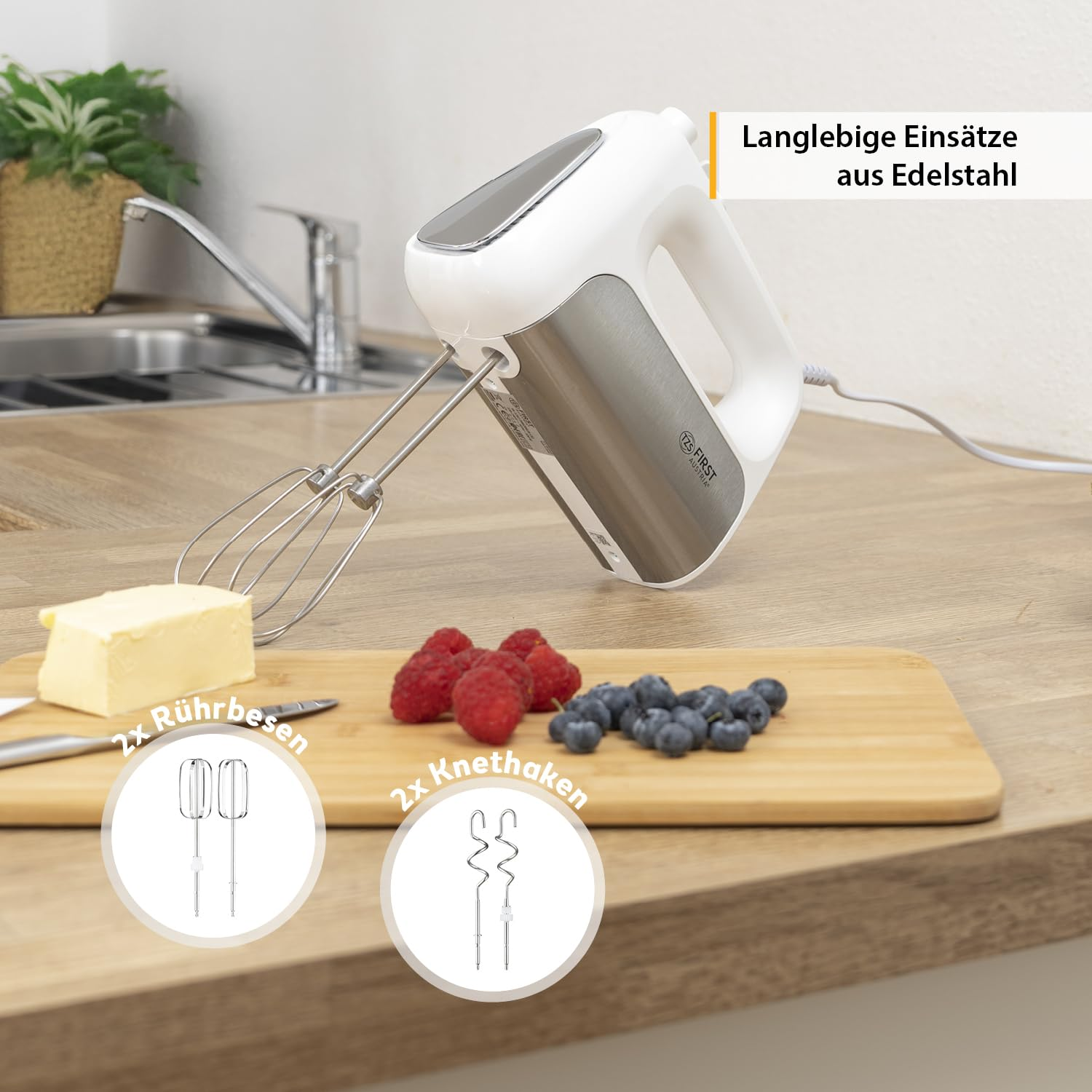 Un mixer a mano bianco e argento su un piano in legno accanto a burro, lamponi e mirtilli su un tagliere.