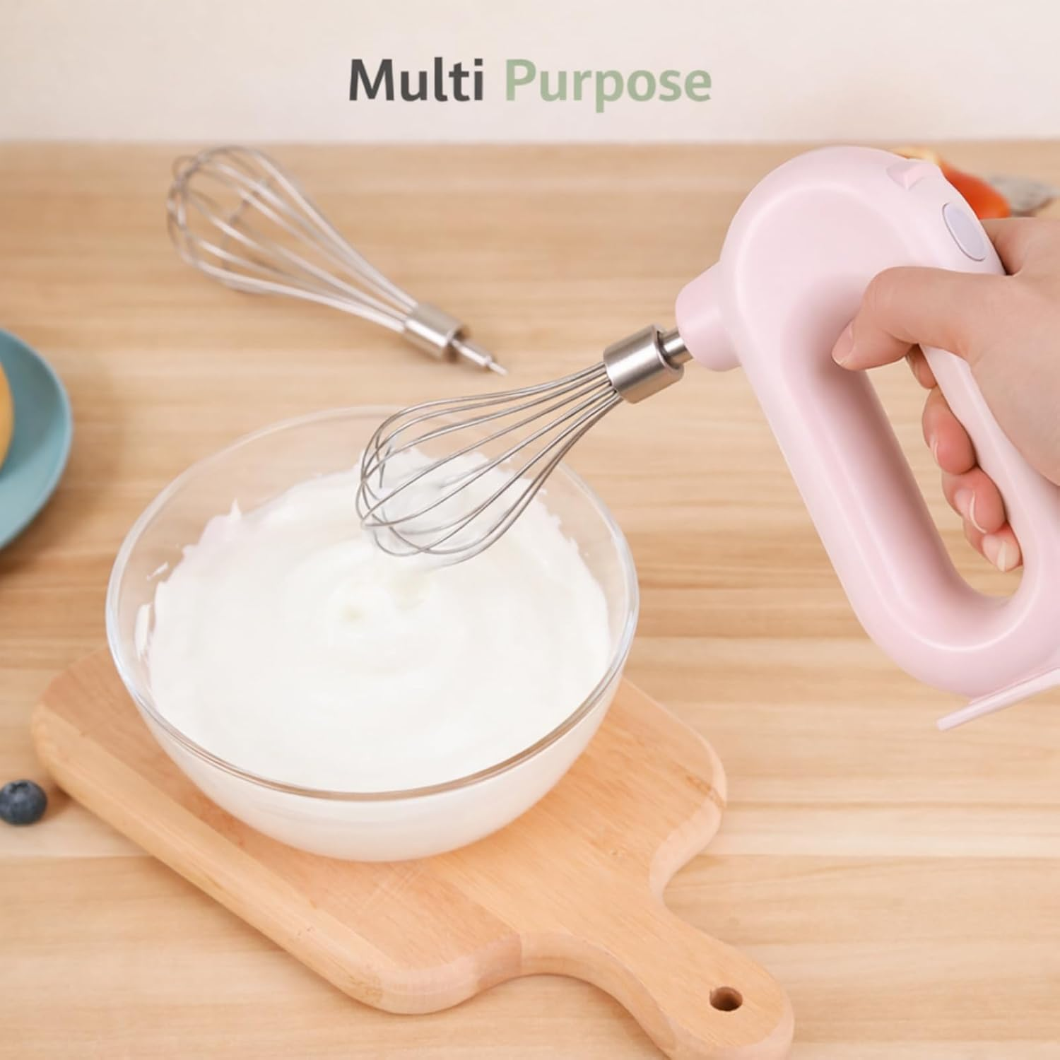 Ein handlicher rosa Mixer rührt weiße Creme in einer Glasschüssel auf einem Holzbrett.