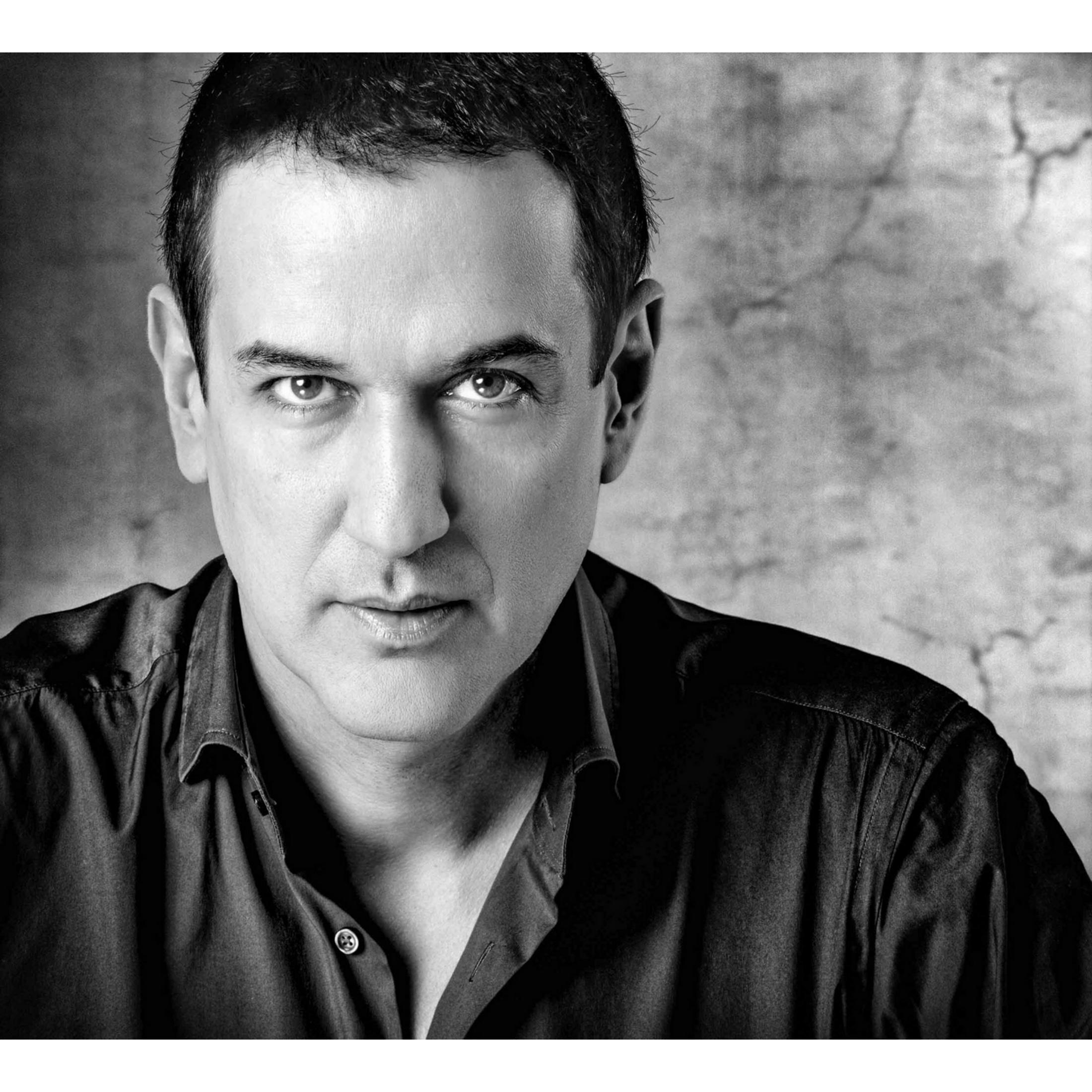 Retrato en blanco y negro de un hombre con camisa oscura sobre fondo texturizado.