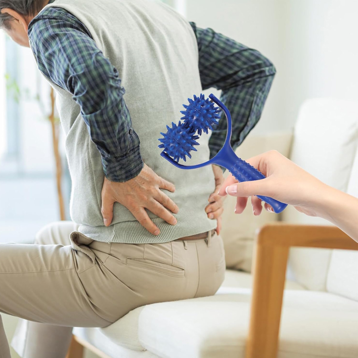Eine Hand hält einen blauen Noppenroller, um dem Rücken eines sitzenden älteren Mannes Massage zu geben.
