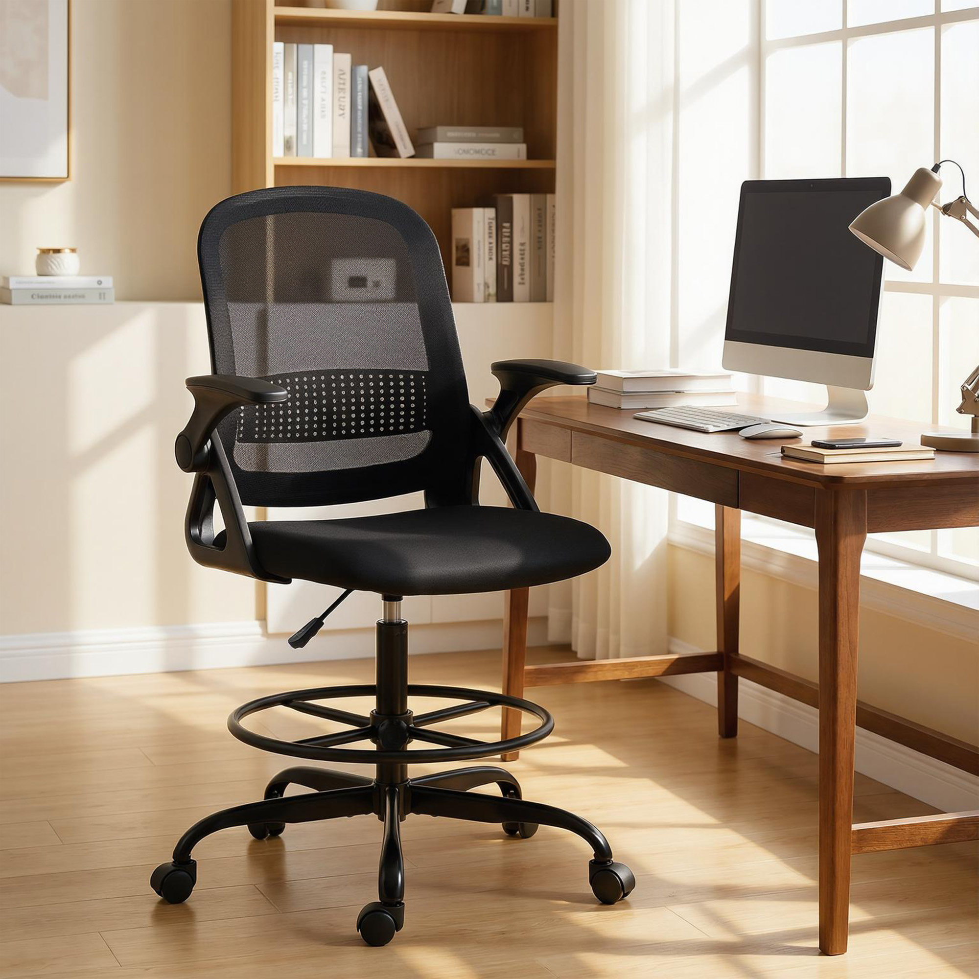 Una sedia da ufficio ergonomica nera con poggiapiedi si trova davanti a una scrivania in legno con computer vicino alla finestra.