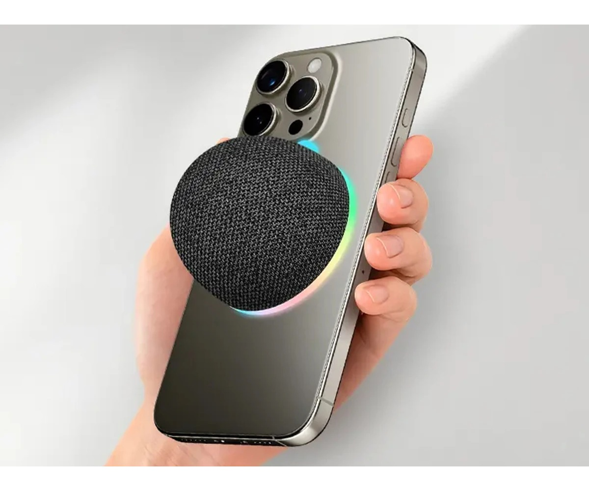 Ręka trzyma srebrny smartfon z okrągłym, szarym głośnikiem z tkaniny z tyłu.