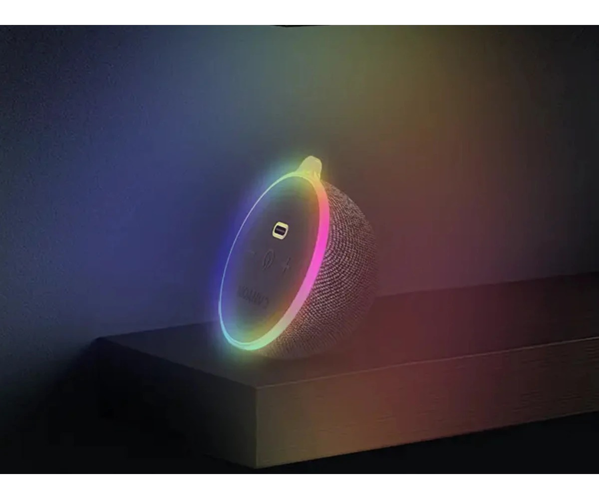 Okrągły głośnik z tkaniny z świecącym pierścieniem RGB LED stoi na półce w ciemnym pokoju.