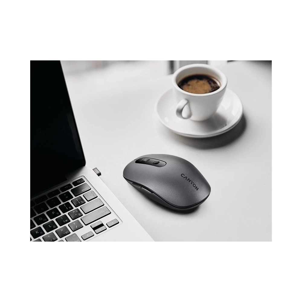 Mysz komputerowa Canyon leży na stole obok laptopa i filiżanki kawy.